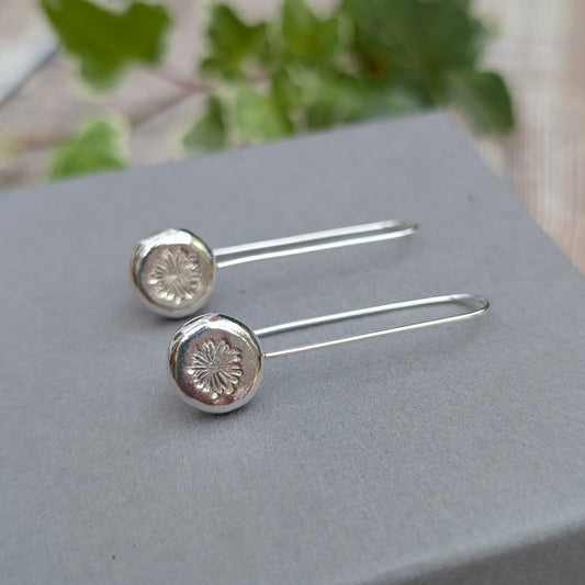 silver daisy pebble long earrings displayed on a grey jewellery box, showing the long handmade ear wires and daisy stamped pebbles.