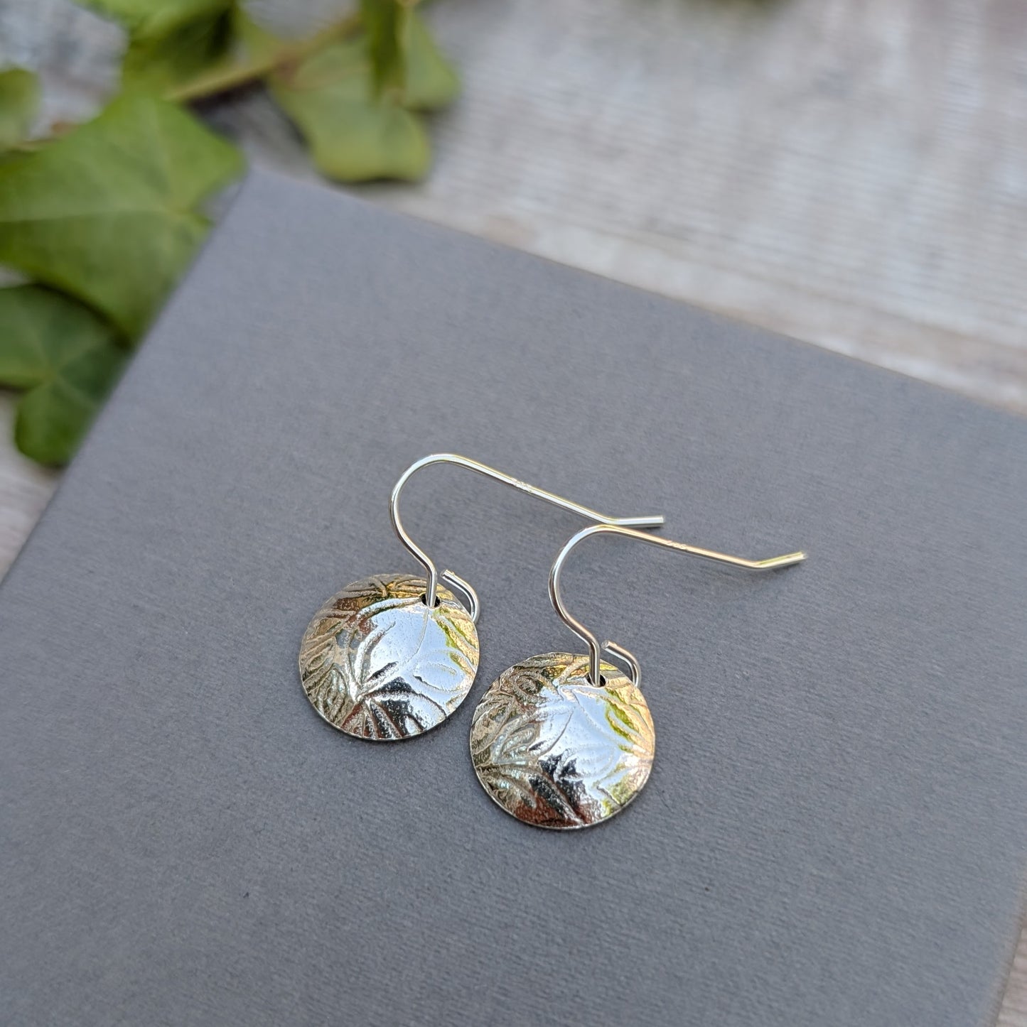 Silver Dome Disc Earrings with Leaf Pattern displayed on a grey surface with natural light.