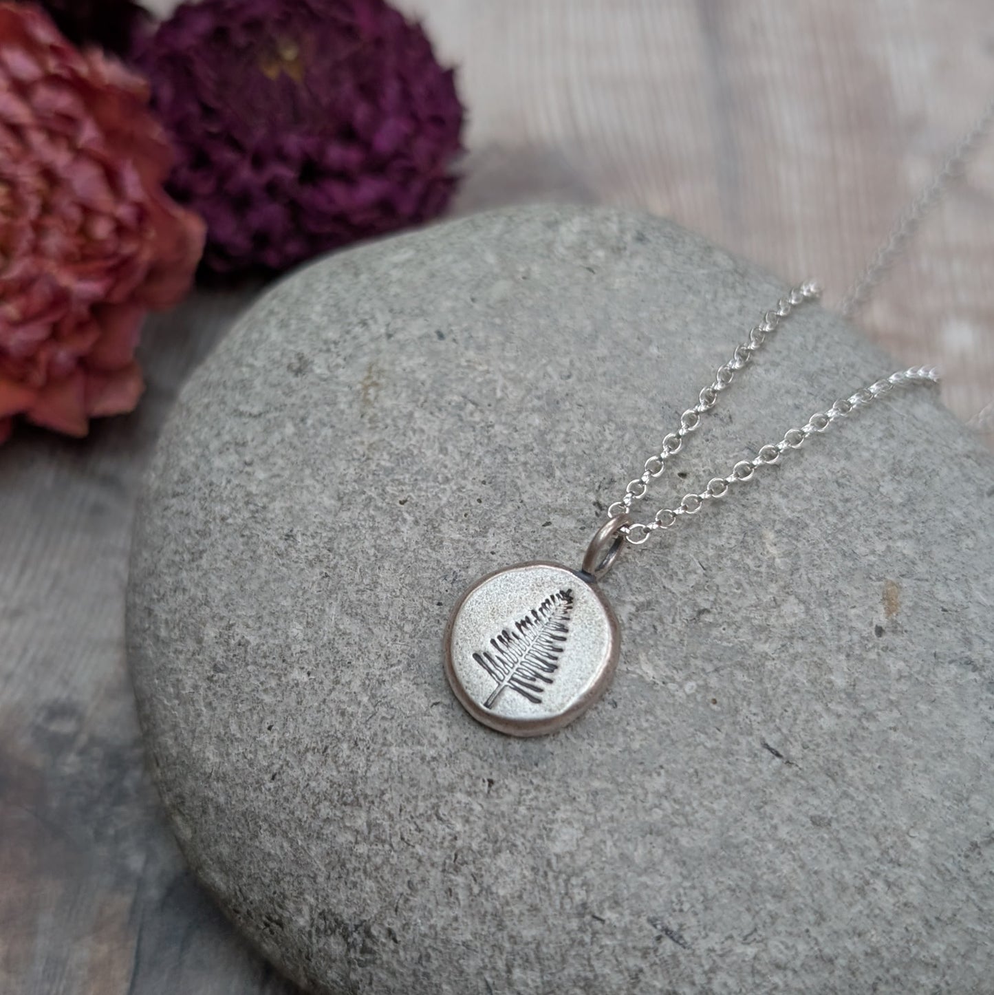Close-up of a silver evergreen tree pebble necklace lying on a stone, highlighting the detailed tree design.