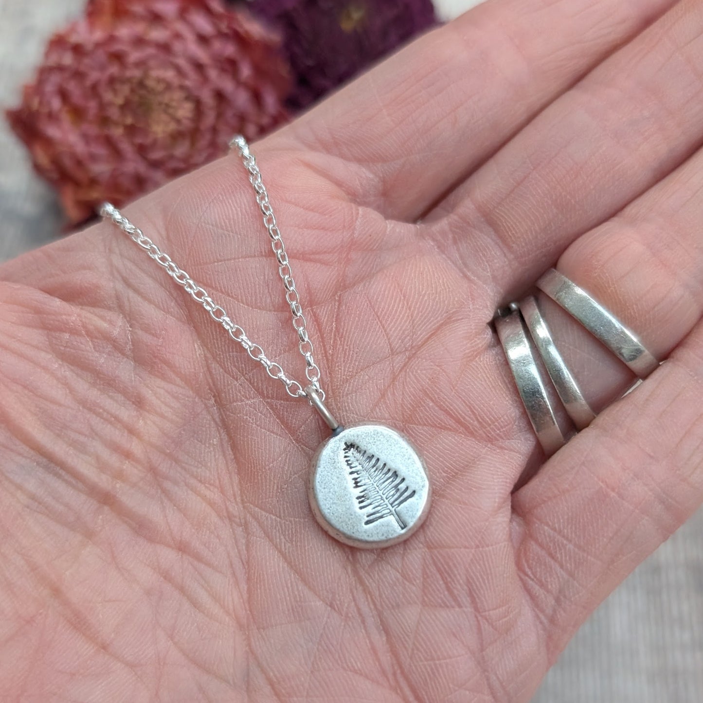 Silver evergreen tree pebble necklace displayed on an open hand, showing the textured round pendant.