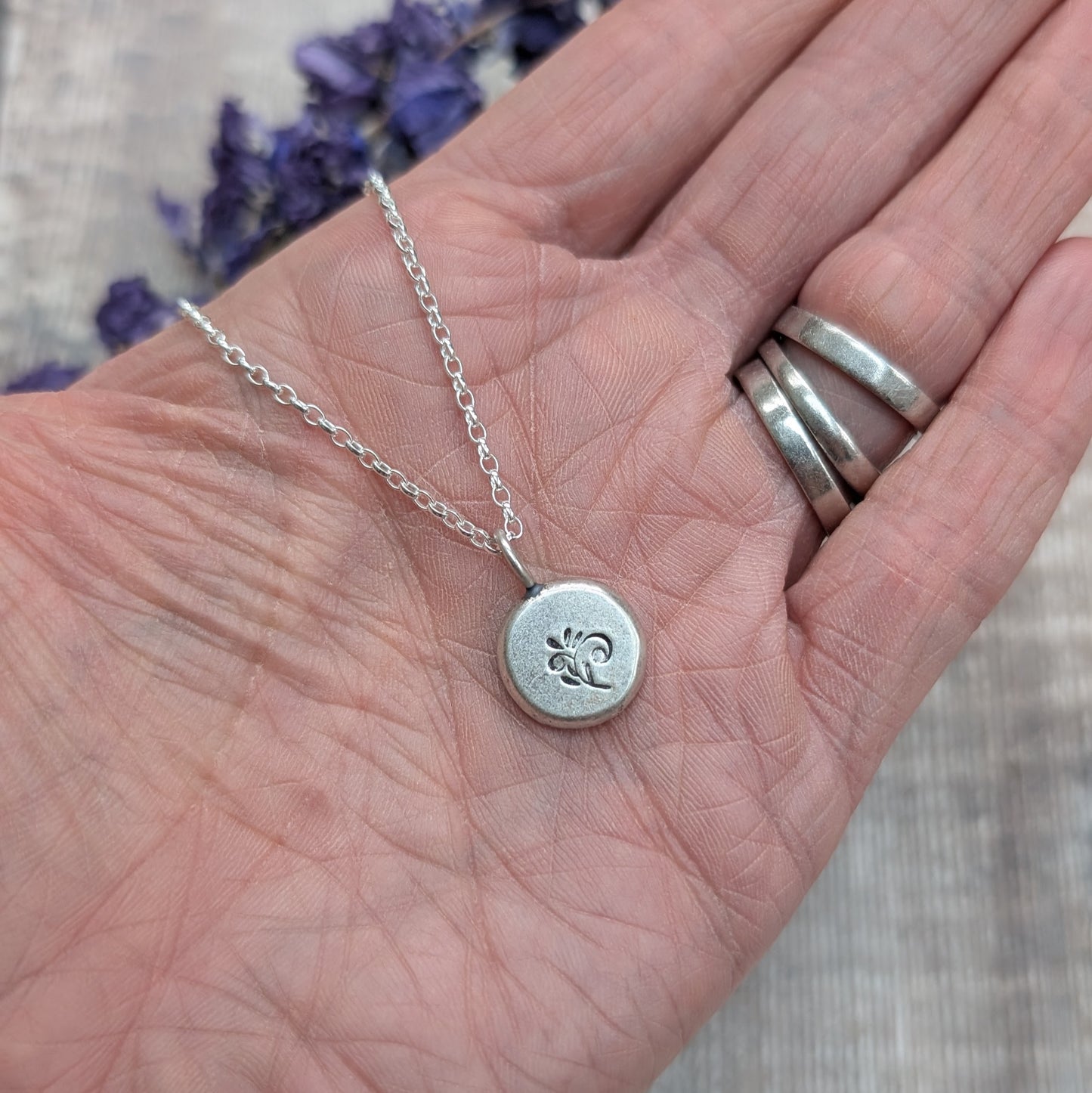 Silver flower pebble necklace displayed on an open hand, highlighting the round pendant and fine chain.