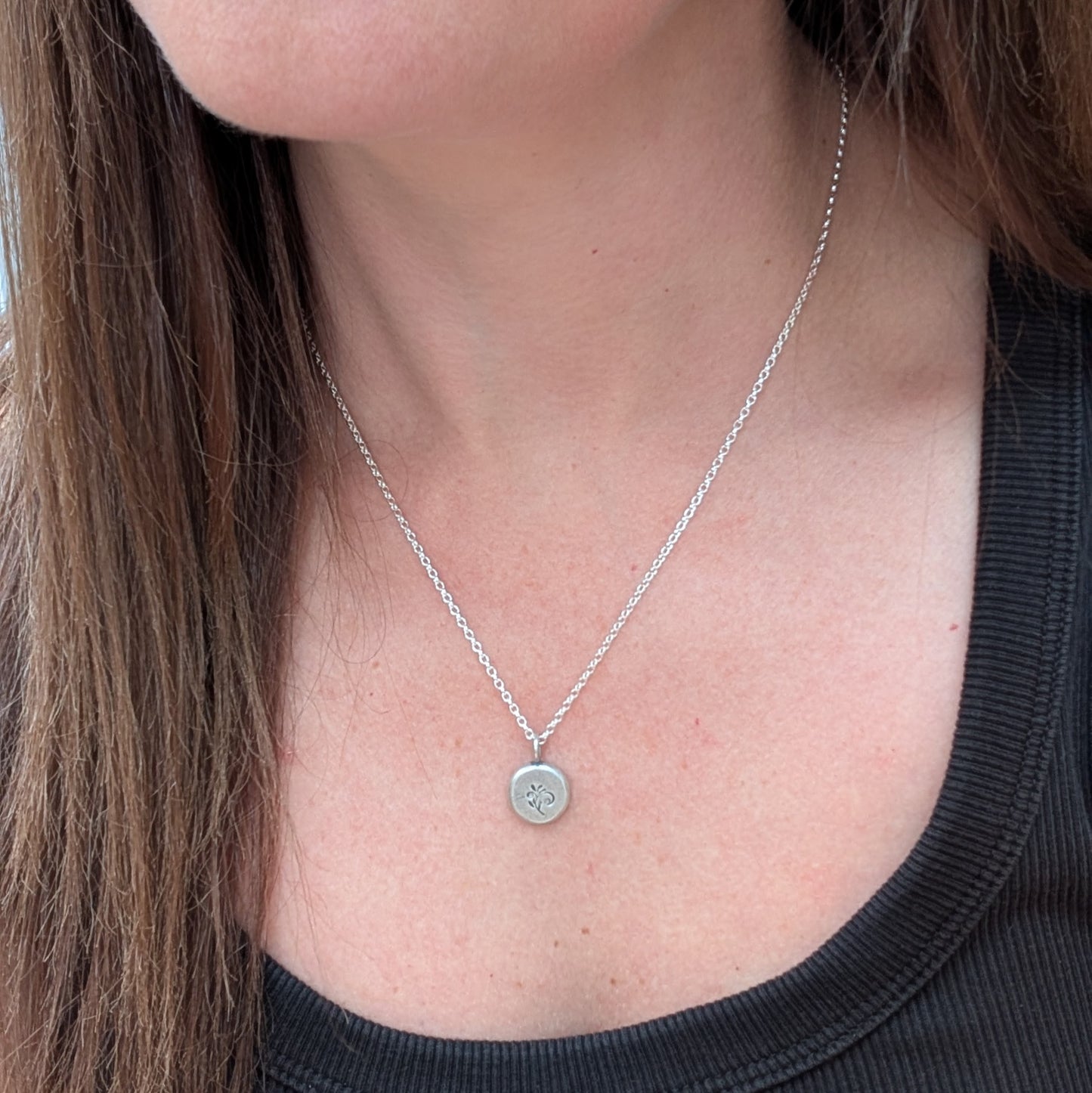 Silver flower pebble necklace being worn, showing the delicate pendant resting at the collarbone.
