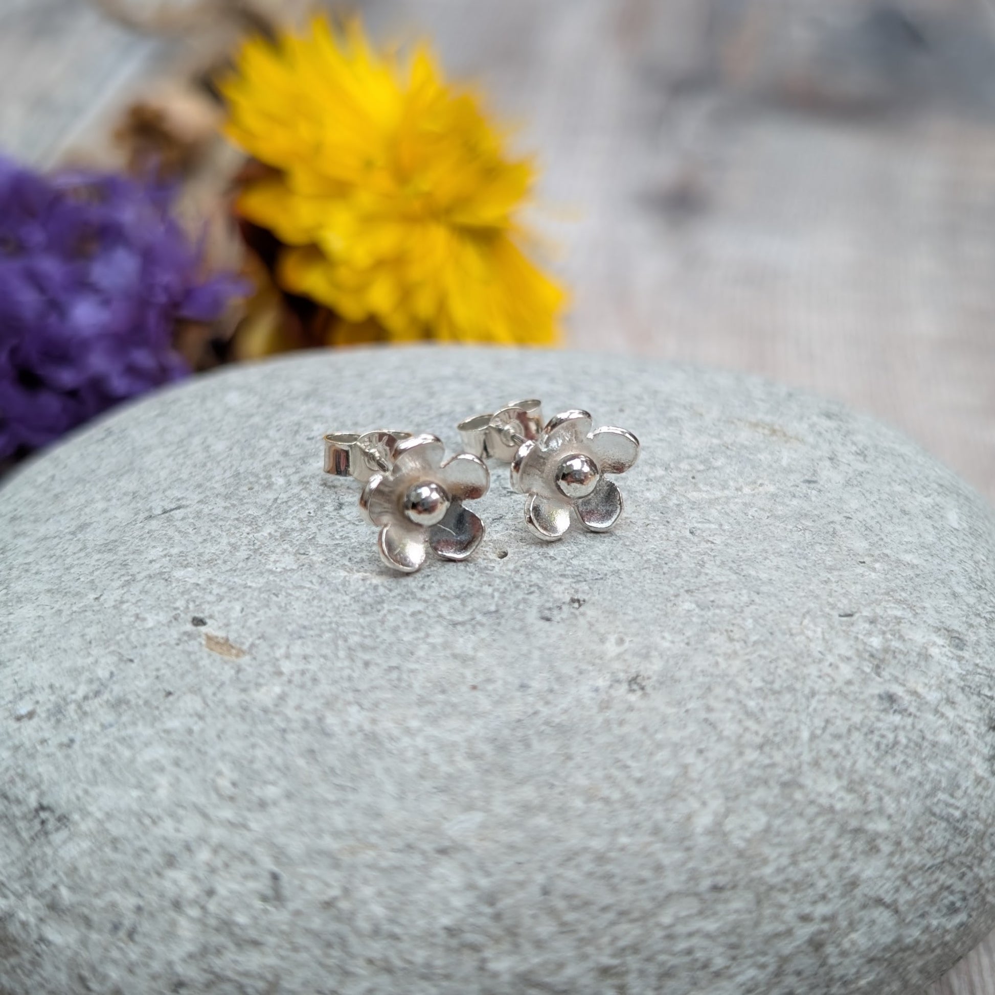 Side view of silver flower stud earrings standing upright on a stone, highlighting the three-dimensional shape of the petals.