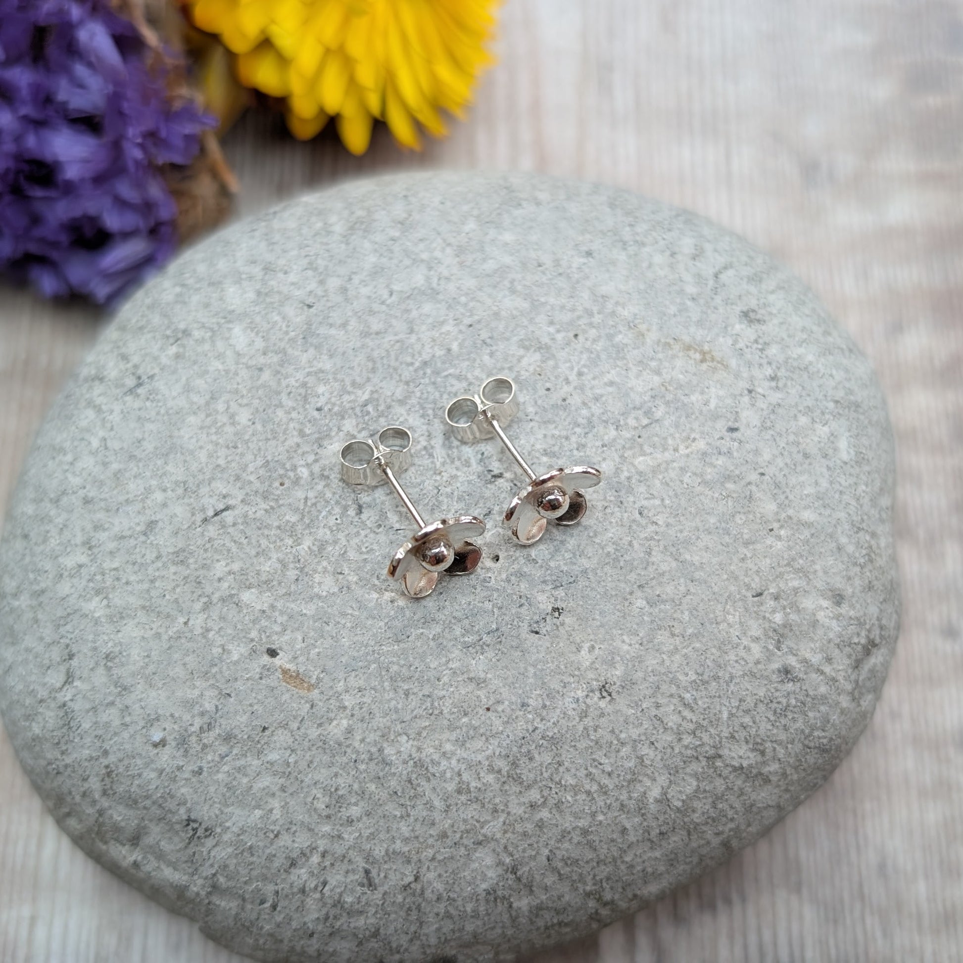 Silver flower stud earrings photographed from the back, showing the stud posts and butterfly backs.