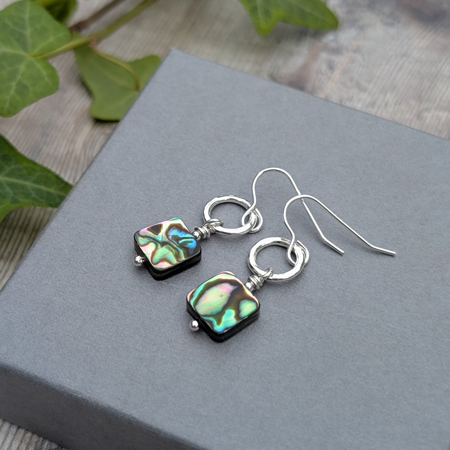 Pair of Silver Hammered Circle Earrings with Abalone Shell Beads on display with greenery and wooden background