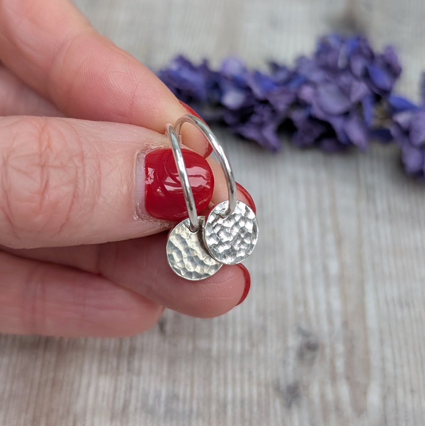 Hand holding Silver Hammered Disc Hoop Earrings close up, showing the reflective hammered surface and minimalist hoop design.