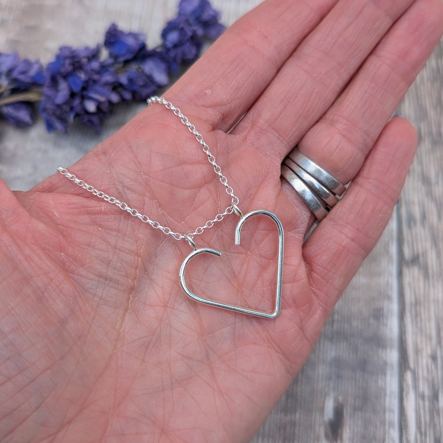 Silver heart ring keeper necklace resting in the palm of a hand, showing the delicate silver chain and heart detail.
