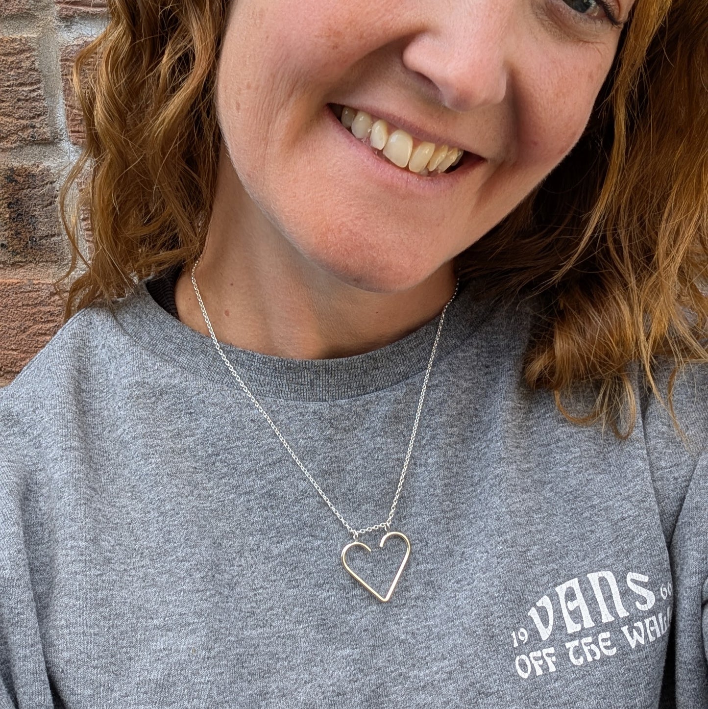 Woman wearing the silver heart ring keeper necklace with a grey t-shirt, the heart pendant resting at the collarbone.