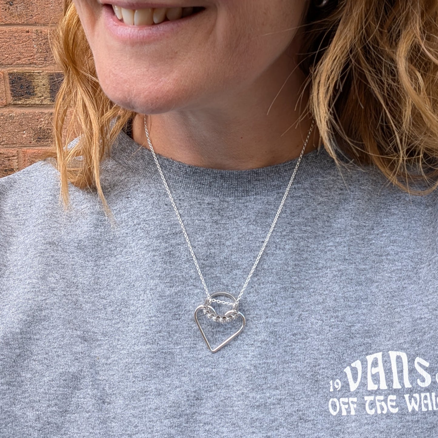 Woman wearing the silver heart ring keeper necklace, styled with a set of silver stacking rings kept safely inside the heart pendant.