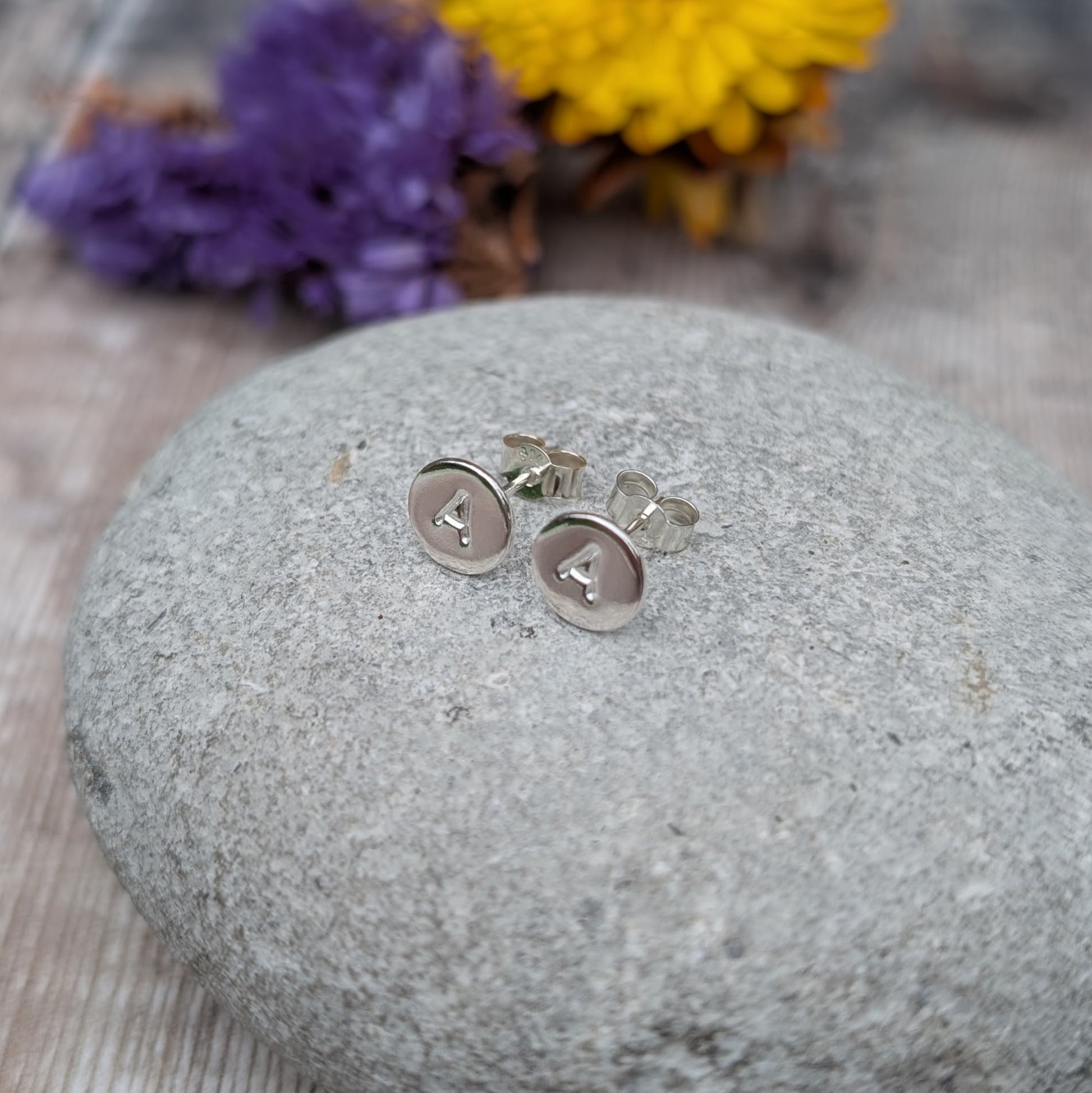 Side view of silver initial stud earrings resting on a grey stone.