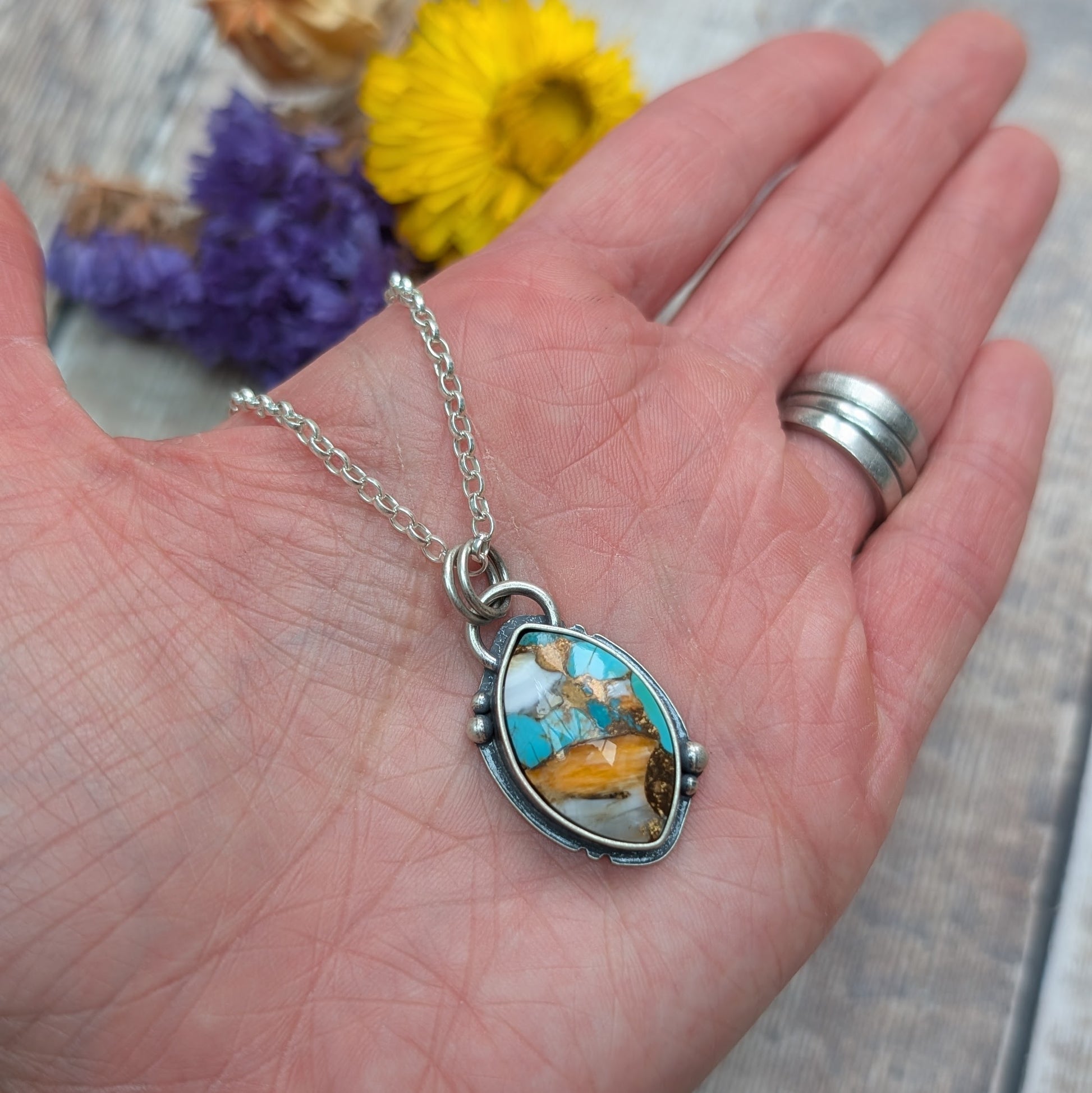 The Silver Kingman Turquoise Necklace shown in an open palm, giving a sense of scale and showcasing the pendant’s rich mix of colours and textured silver frame.