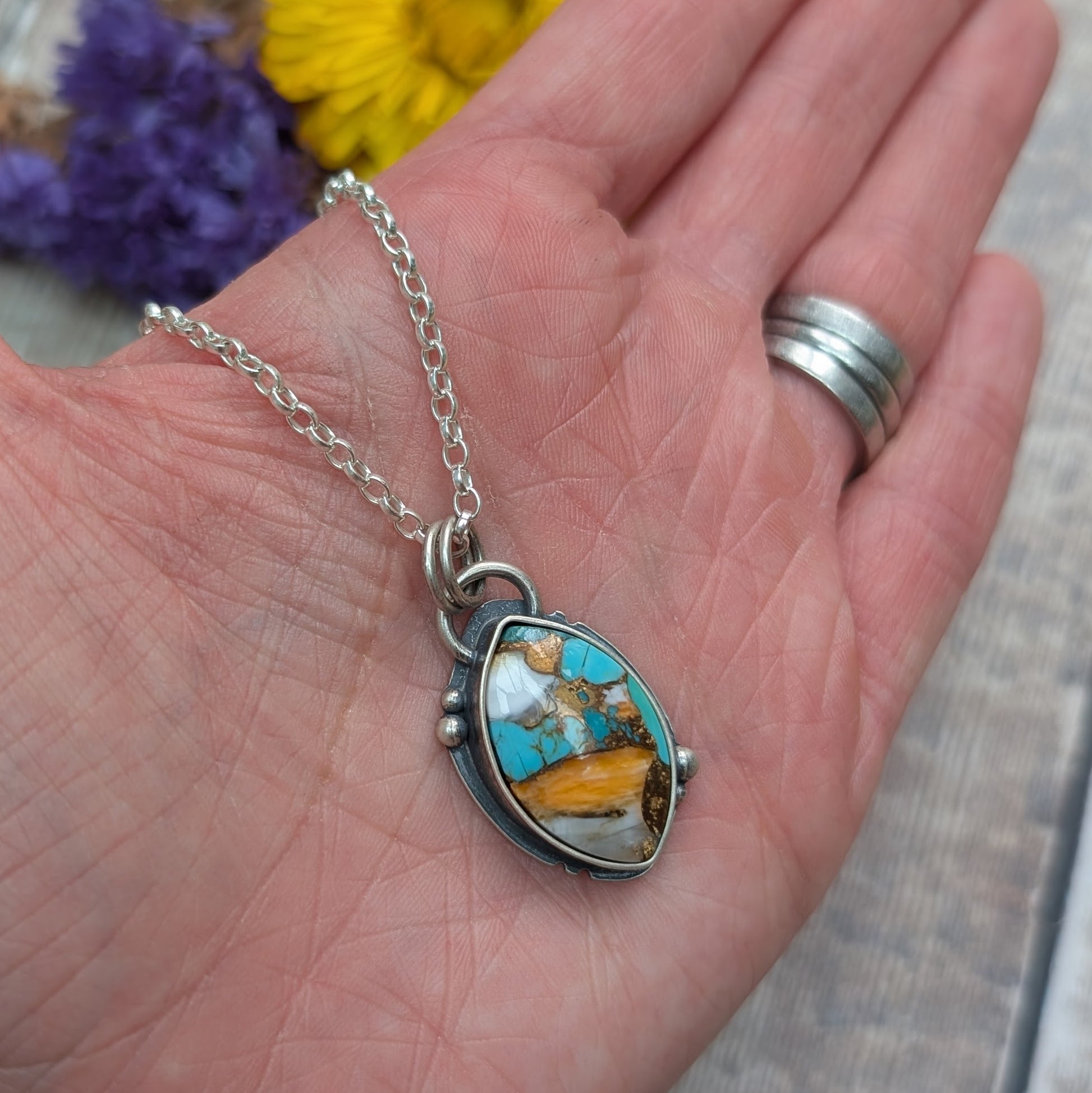 The Silver Kingman Turquoise Necklace shown in an open palm, giving a sense of scale and showcasing the pendant’s rich mix of colours and textured silver frame.