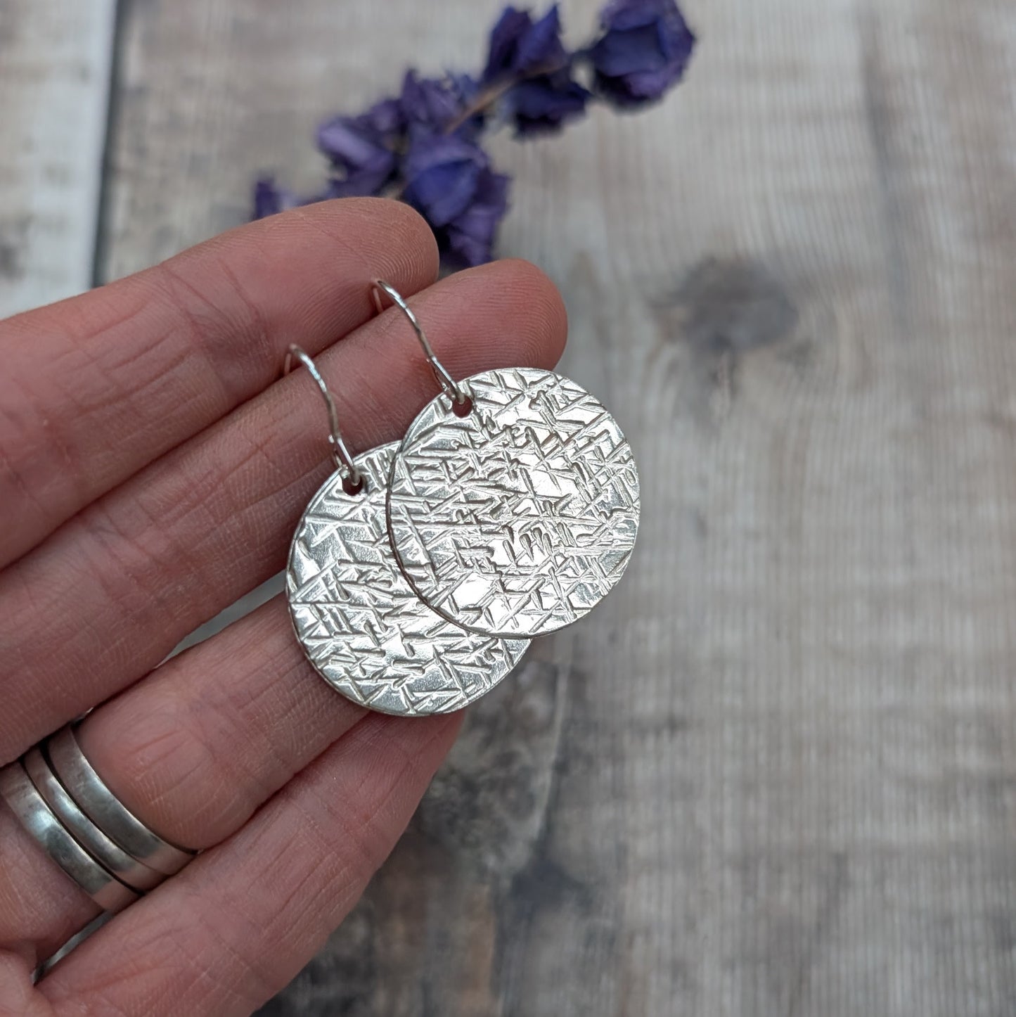 Hand holding silver large textured hammered disc earrings with a bright hammered pattern catching the light.