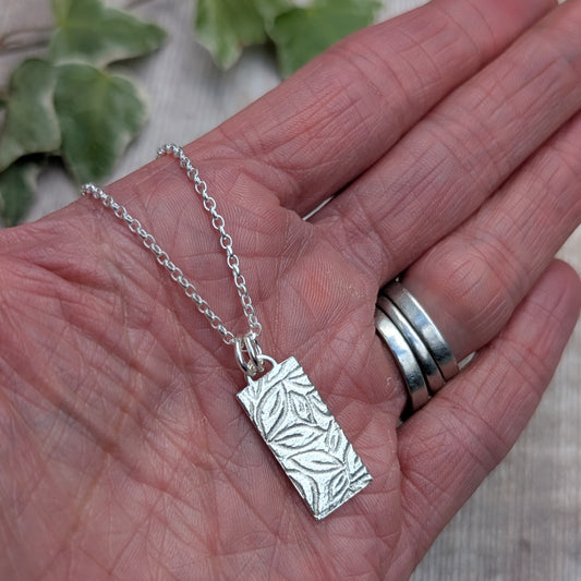 Silver leaves rectangle necklace handmade from recycled Sterling Silver, shown resting in a hand to show the size and detailed leafy pattern.