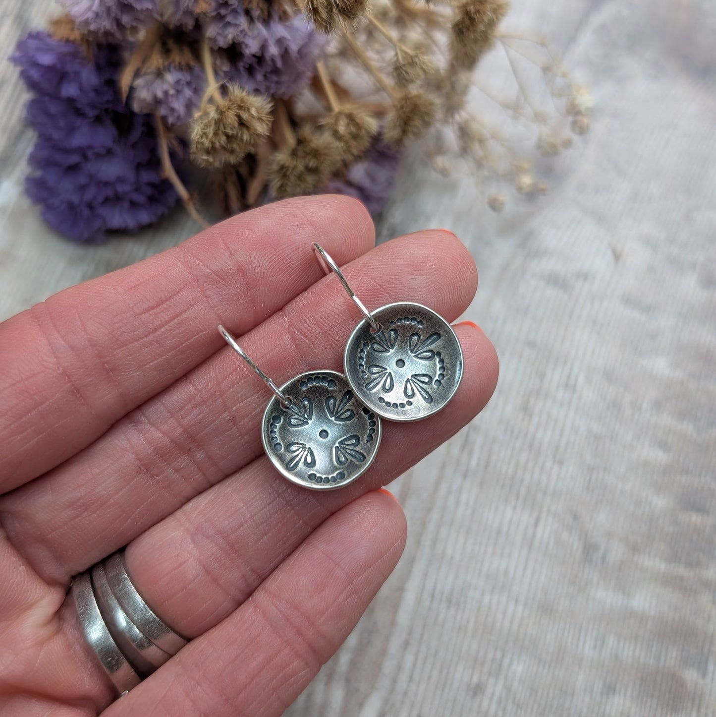 The Silver Mandala Dome Disc Earrings displayed on a person's fingers, highlighting their small size and the delicate oxidised pattern.