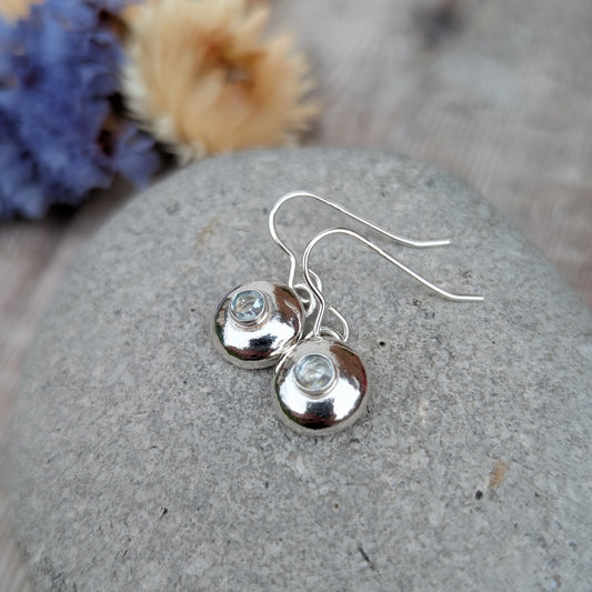 Silver pebble earrings with Aquamarine resting on a smooth grey stone.