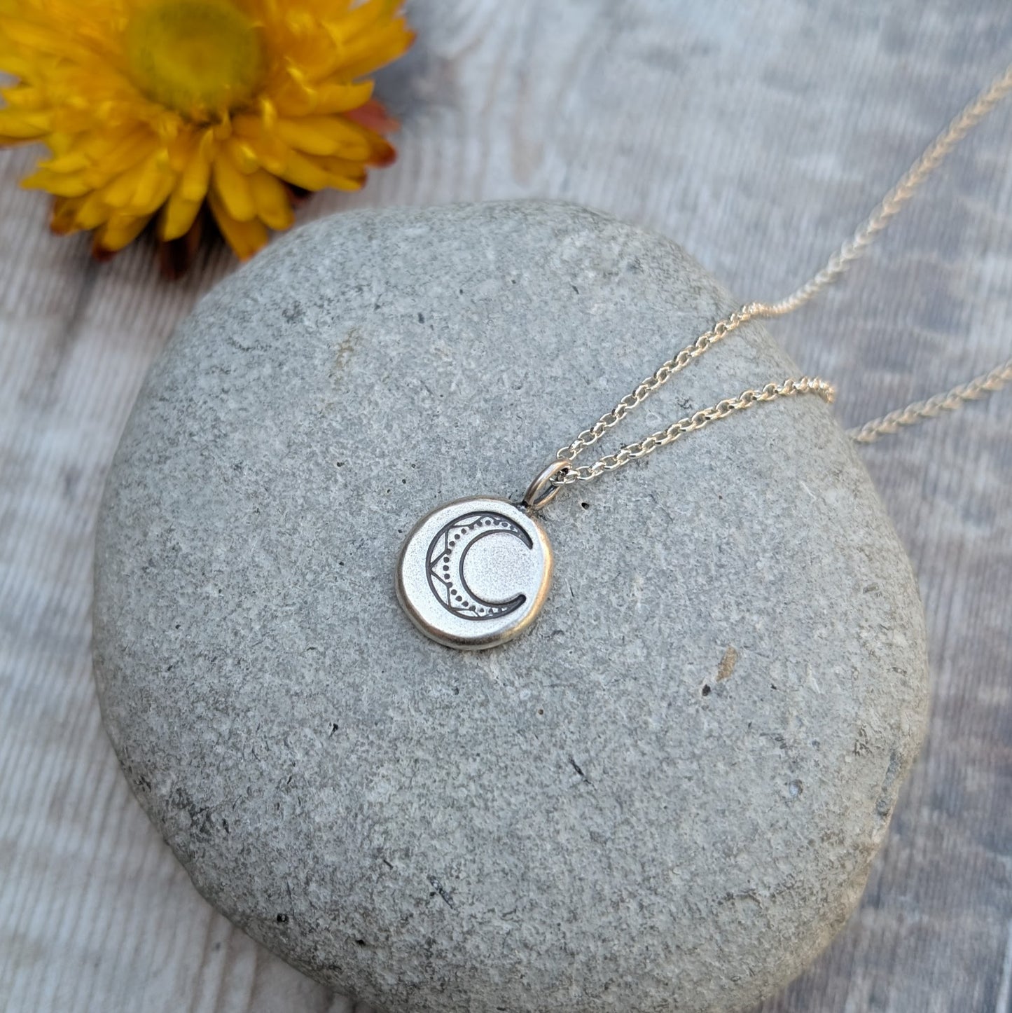 Silver Pebble Stamped Moon Necklace lying on a grey stone, showing the hand-stamped crescent moon detail clearly.