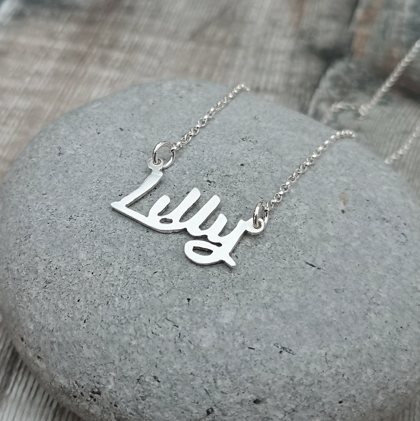 silver personalised name necklace shown displayed on a grey stone.