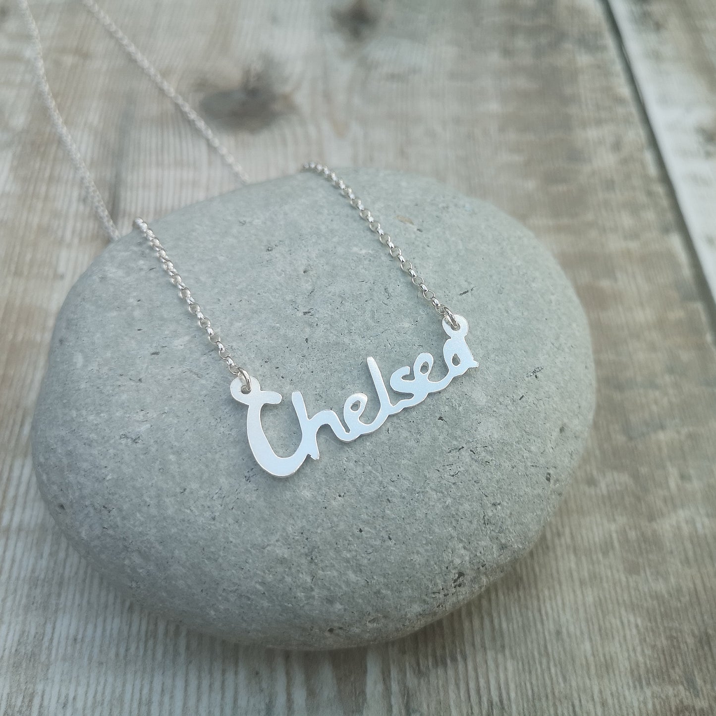 silver personalised name necklace shown displayed on a grey stone.