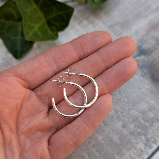 Silver smooth hoop earrings handmade from recycled Sterling Silver resting in the palm of a hand to show their size.