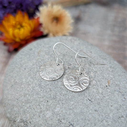 Silver Spiral Pattern Disc Earrings resting on a stone, showing hand cut discs with spiral pattern detail