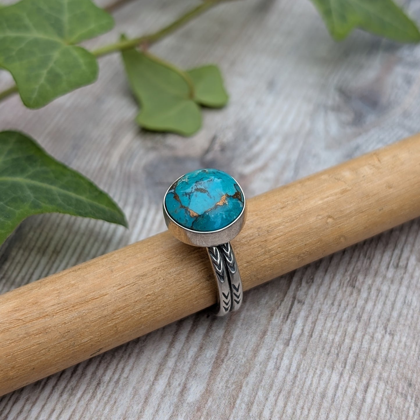 Silver Sunburst Stamped Ring with Turquoise displayed on wooden surface with green ivy background