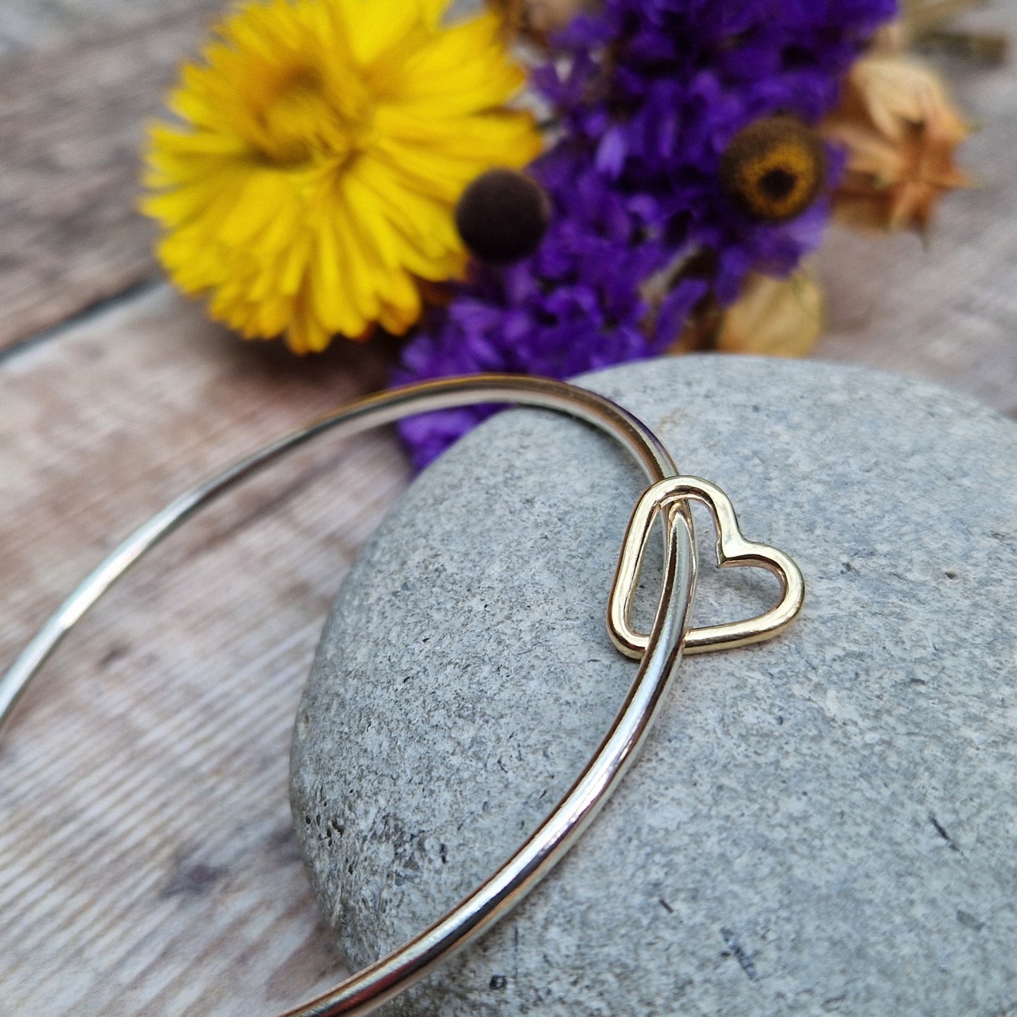 Sterling Silver bangle passes through a smaller a 9ct Gold open heart shape. Heart moves independently around the bangle.