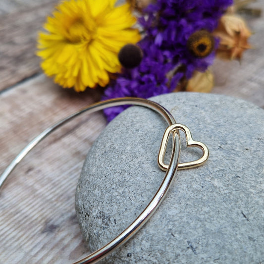 Sterling Silver bangle passes through a smaller a 9ct Gold open heart shape. Heart moves independently around the bangle.