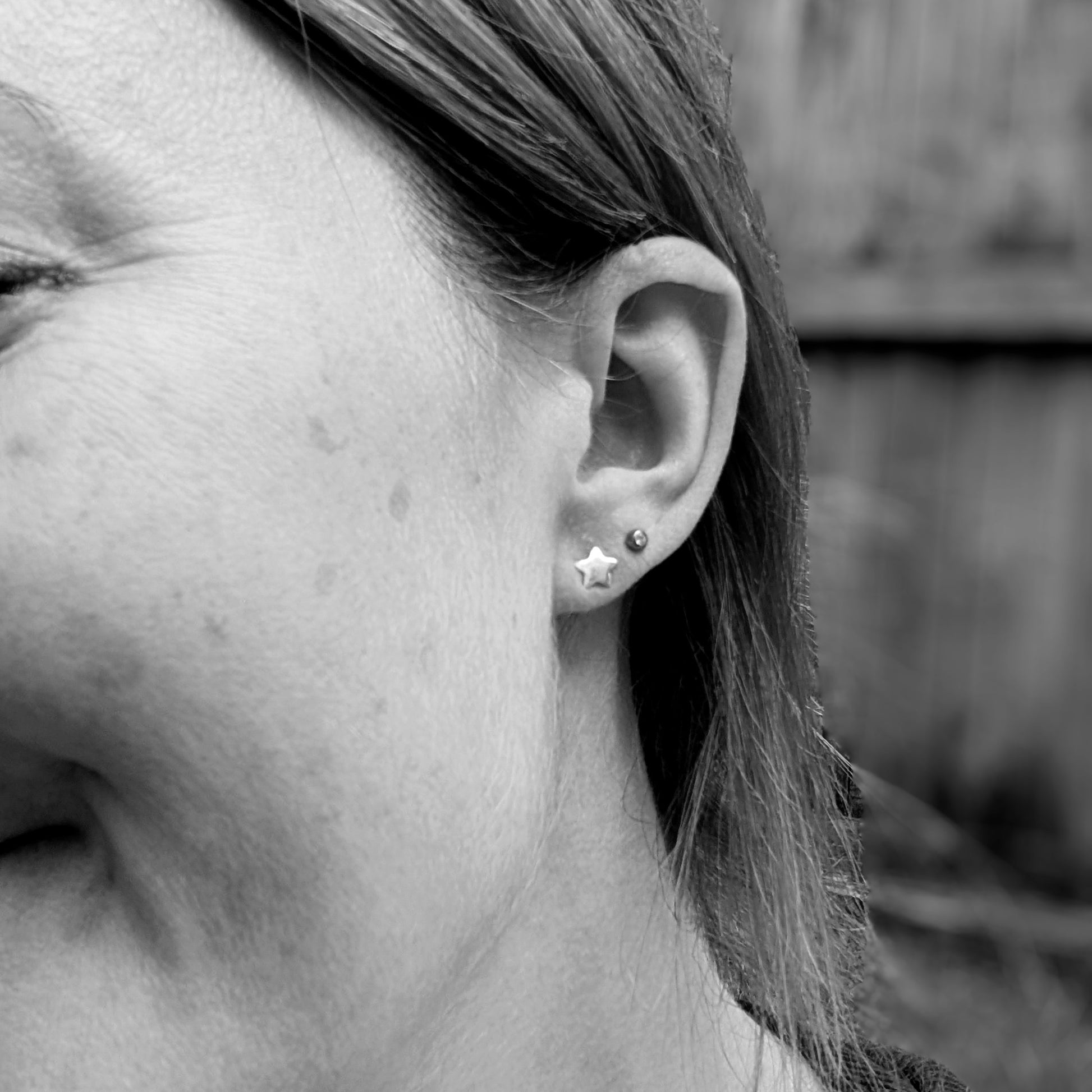 Black and white image of a person wearing a small silver star stud earring in the earlobe, showing the earring's size and placement.