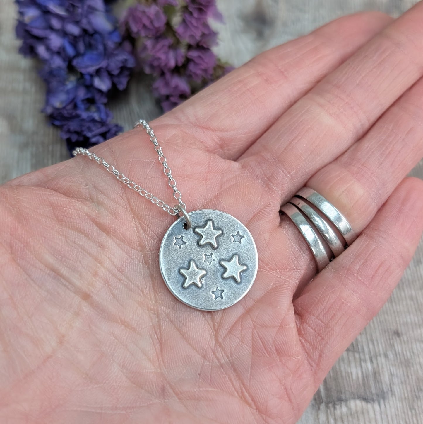 A pair of recycled sterling silver and copper star stud earrings held in a hand, showcasing their small, organic shape. Each silver pebble is formed by melting scrap silver, with a contrasting copper star. Sustainable, handmade jewellery for everyday wear.