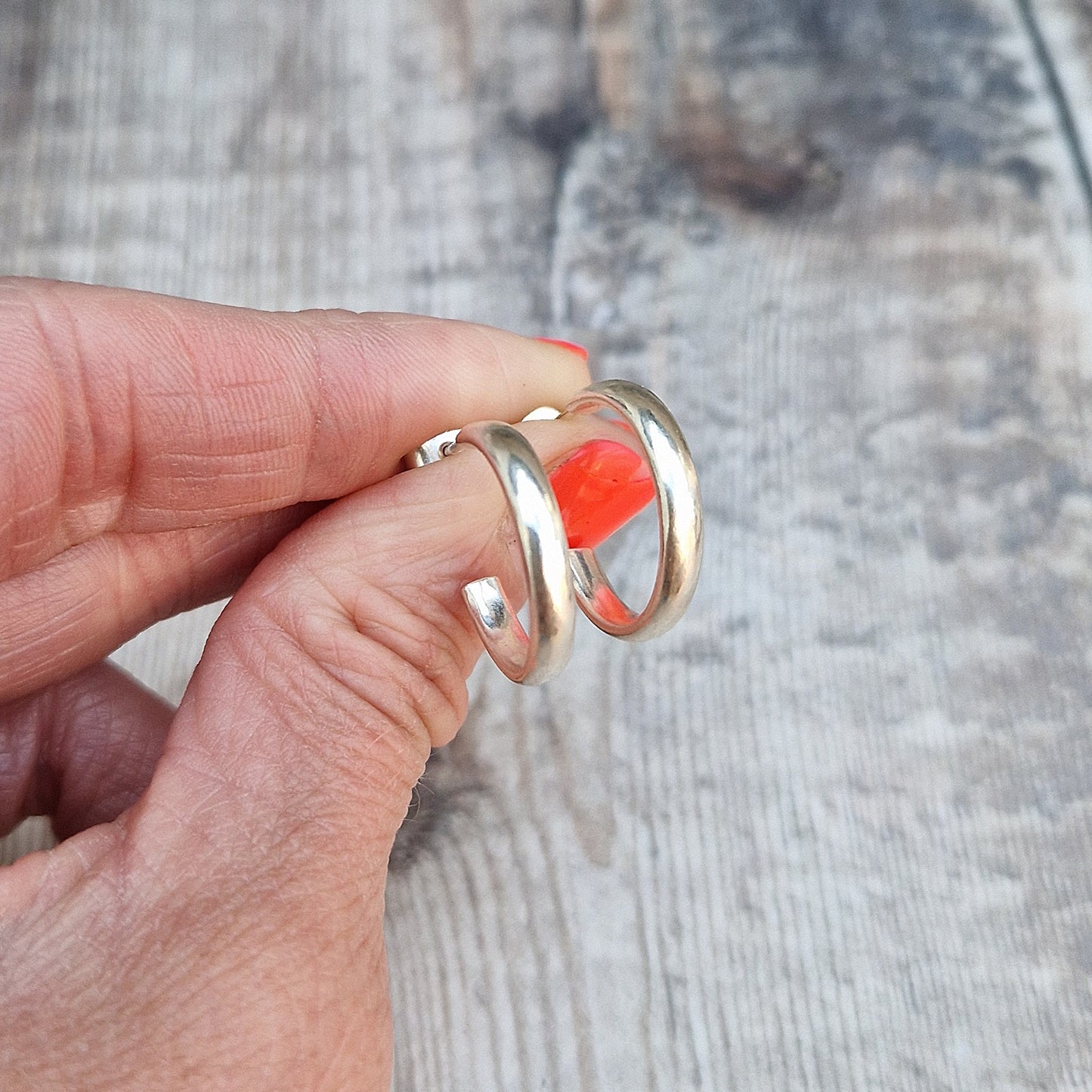 A hand holding a pair of sterling silver oval wire hoop earrings, showcasing their smooth, polished finish.
