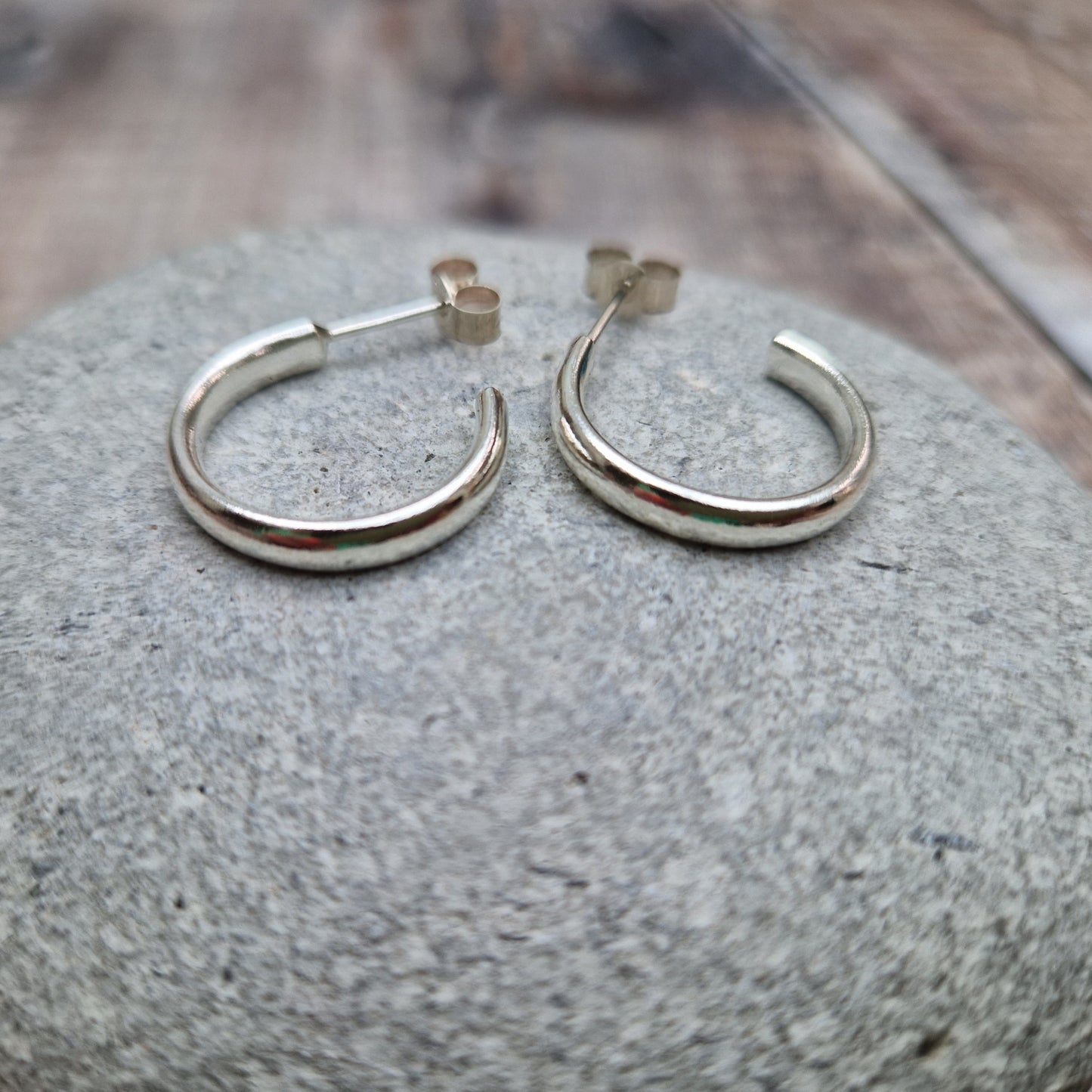 A pair of sterling silver oval wire hoop earrings displayed on a smooth stone surface, highlighting their elegant curved design.