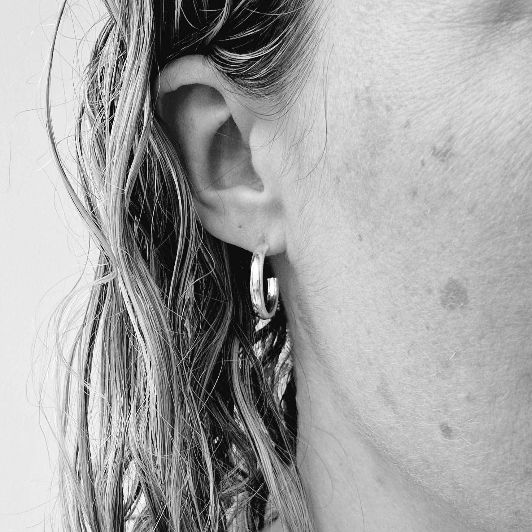 Black and white image of a person wearing a sterling silver oval wire hoop earring, showing how it sits on the earlobe.