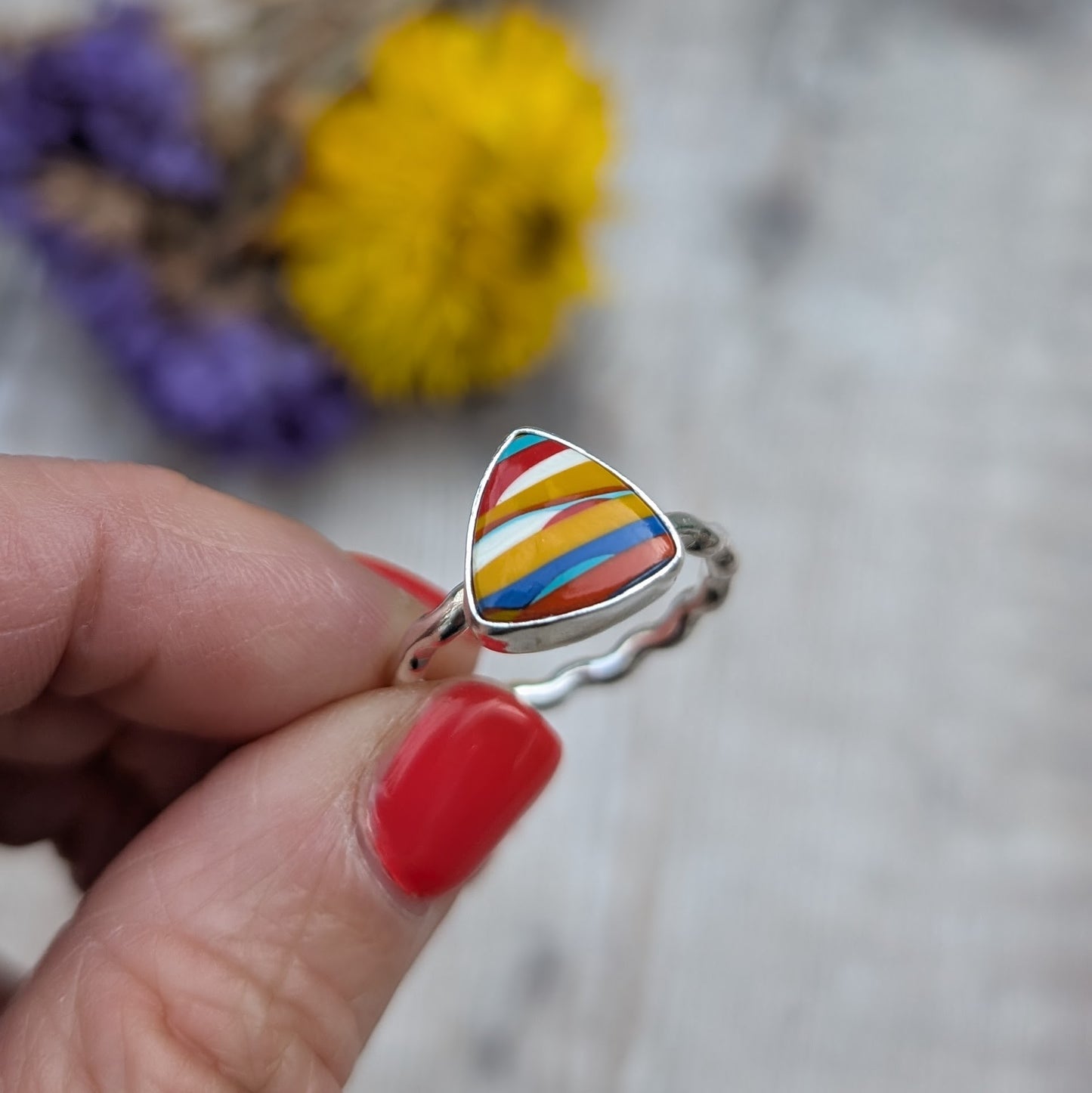 A hand holding the Surfite ring to show its colourful stripes and wave-textured silver band.