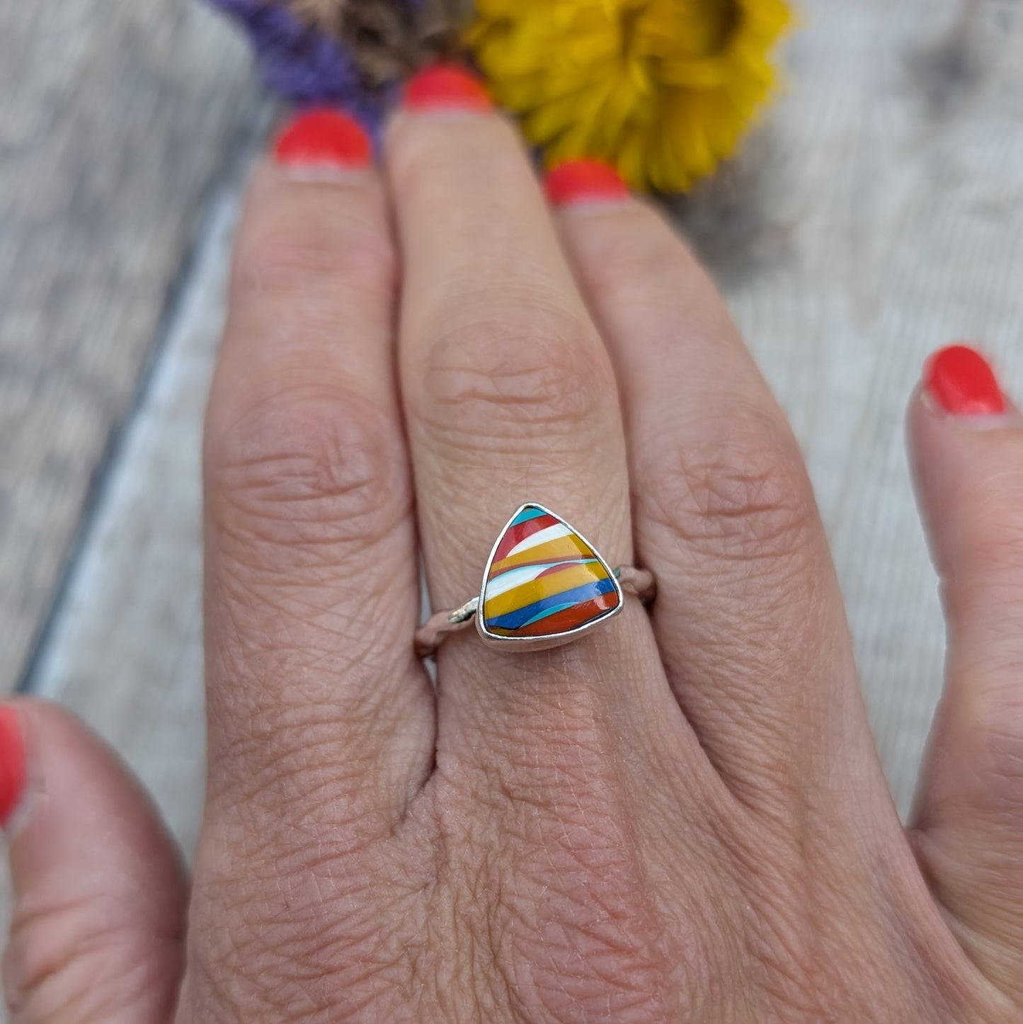 A close-up of a hand wearing a recycled sterling silver ring with a colourful triangular Surfite stone.