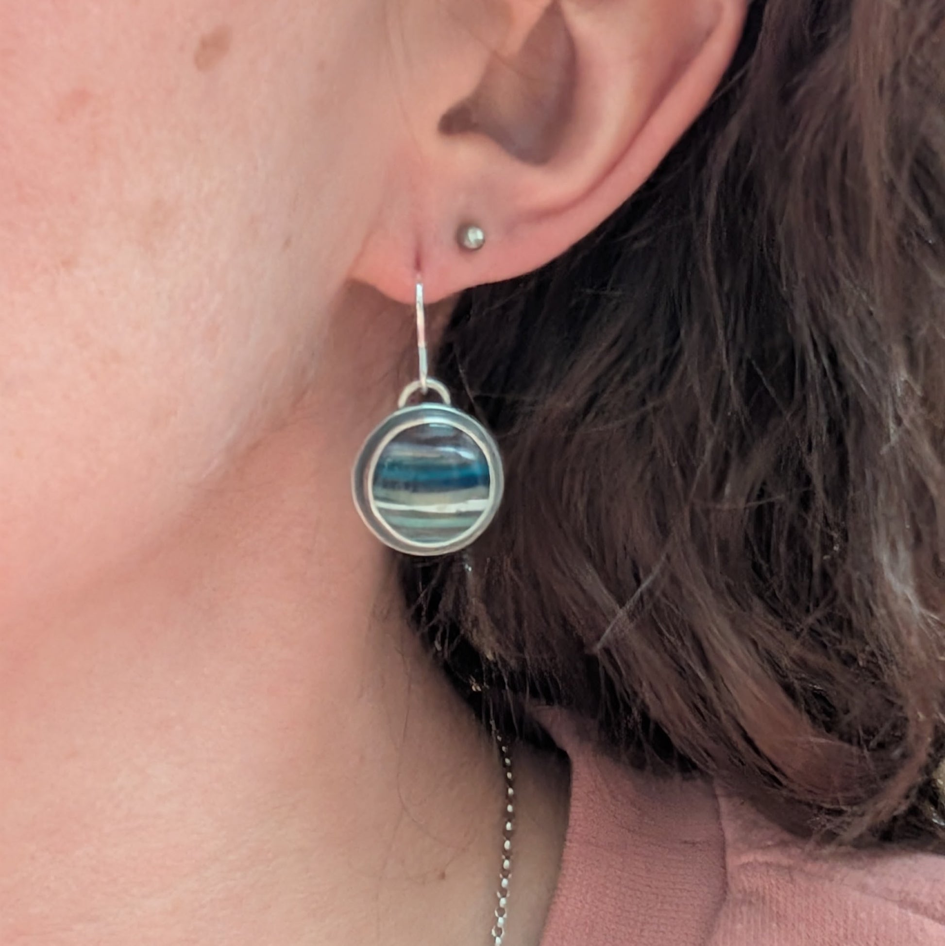 Each earring is a round surfite stone set in an oxidised silver bezel, suspended from silver earring wire. Surfite has random horizontal uneven stripes of lilac, blue, turquoise, green, white and black, gloss finish.