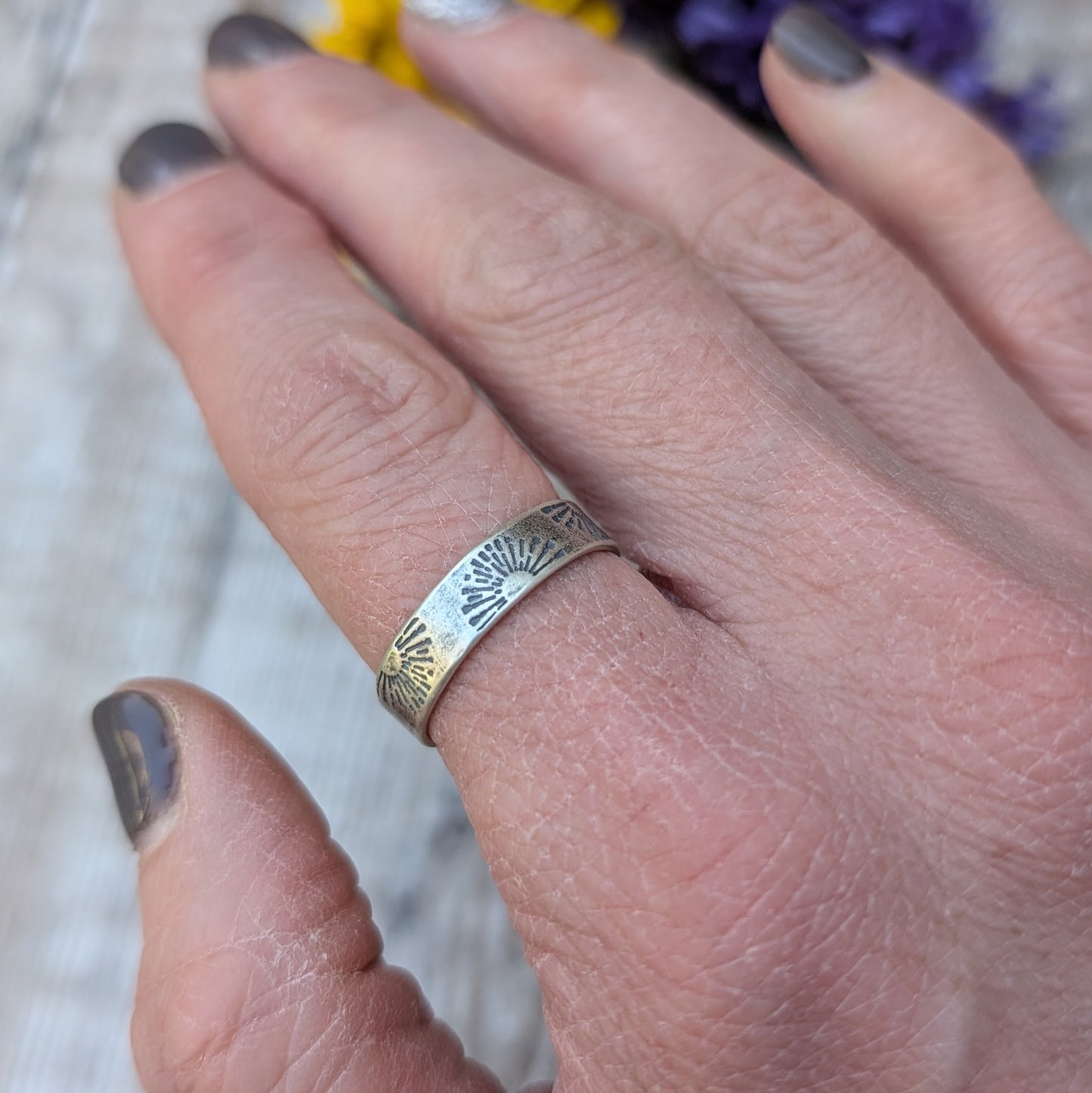 A hand wearing an oxidised silver ring with a stamped sunburst design, showcasing the comfortable fit and rustic finish.