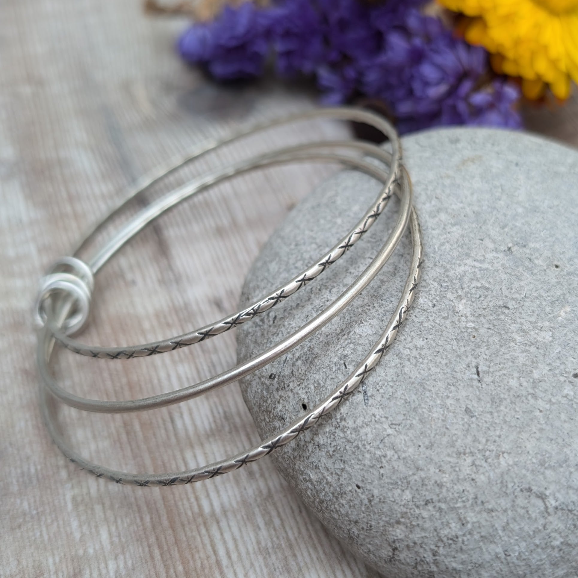 Three Sterling Silver bangles, one patterned, one smooth, one patterned passing through three silver open circles that move independently around the bangles.