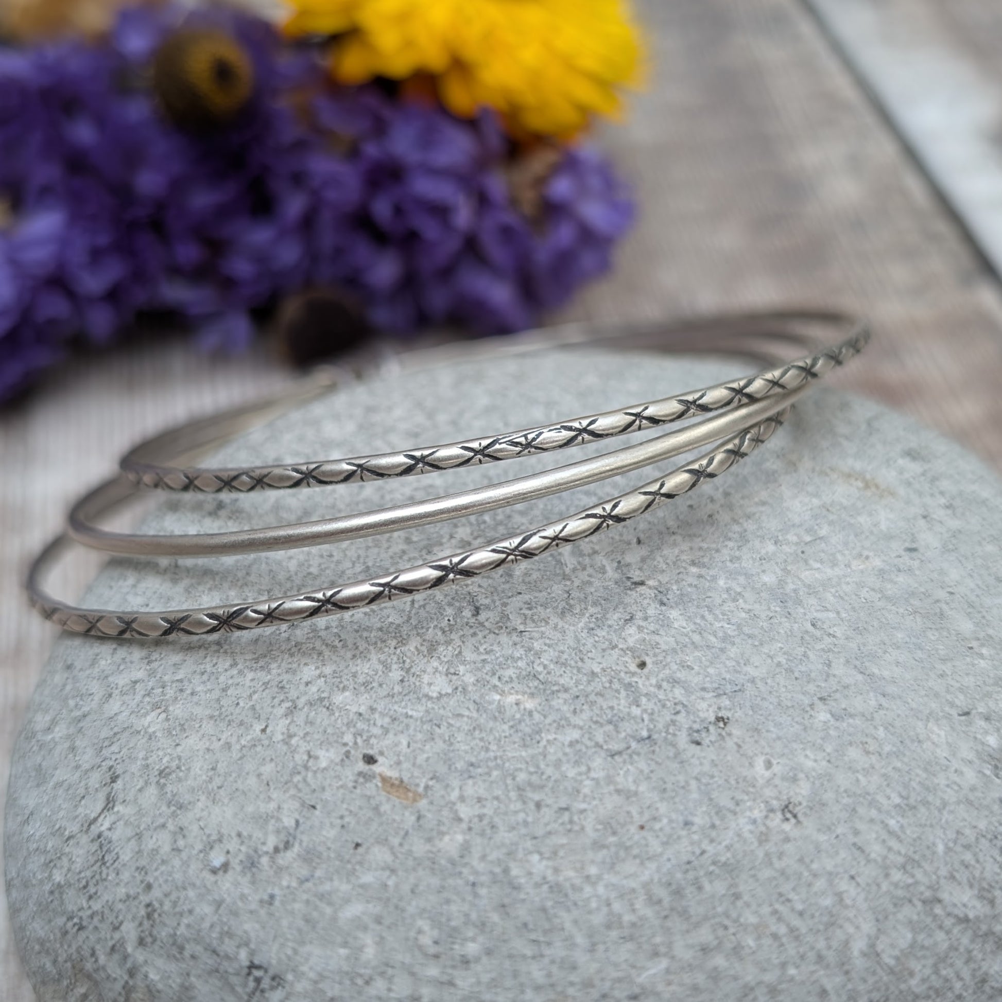 Three Sterling Silver bangles, one patterned, one smooth, one patterned passing through three silver open circles that move independently around the bangles.