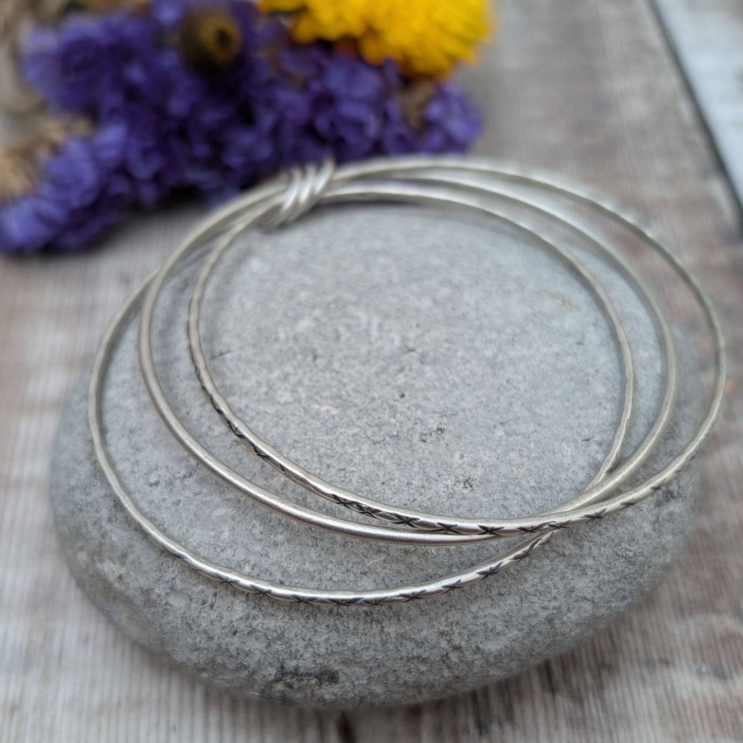 Three Sterling Silver bangles, one patterned, one smooth, one patterned passing through three silver open circles that move independently around the bangles.