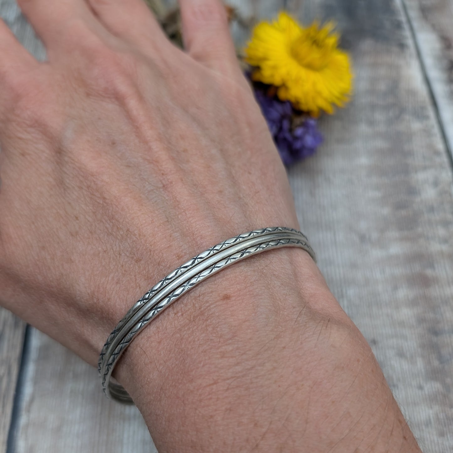 Three Sterling Silver bangles, one patterned, one smooth, one patterned passing through three silver open circles that move independently around the bangles.
