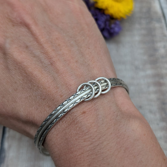 Three Sterling Silver bangles, one patterned, one smooth, one patterned passing through three silver open circles that move independently around the bangles.