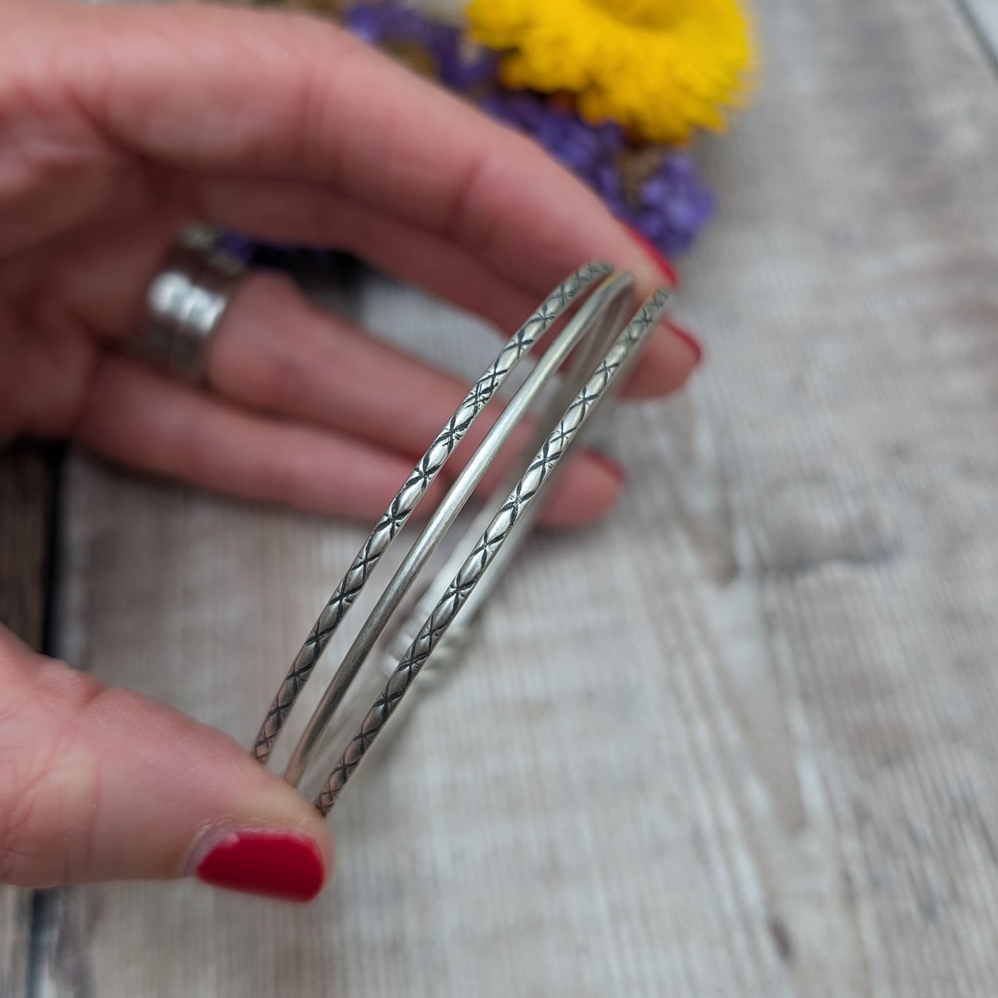 Three Sterling Silver bangles, one patterned, one smooth, one patterned passing through three silver open circles that move independently around the bangles.