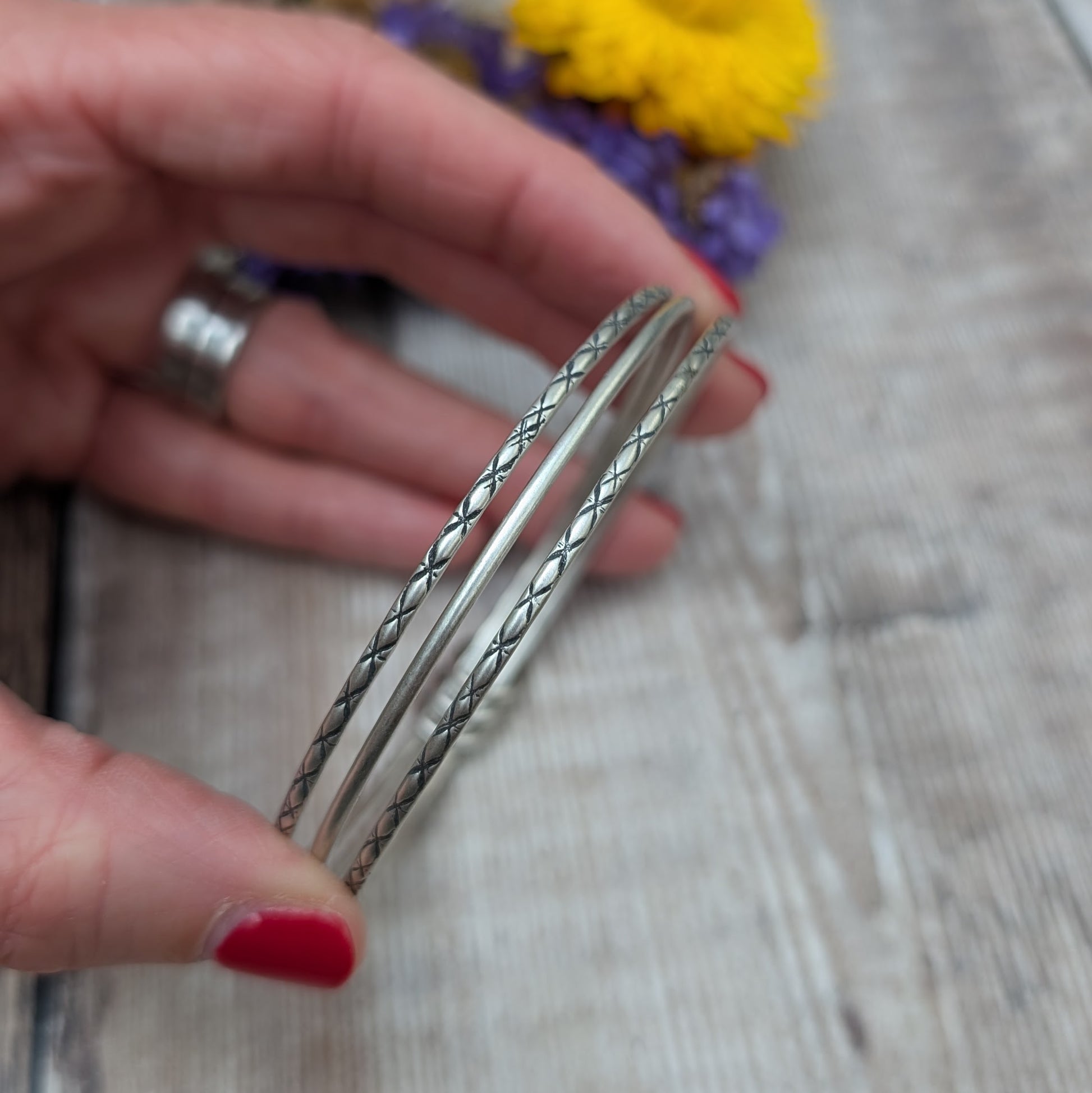 Three Sterling Silver bangles, one patterned, one smooth, one patterned passing through three silver open circles that move independently around the bangles.