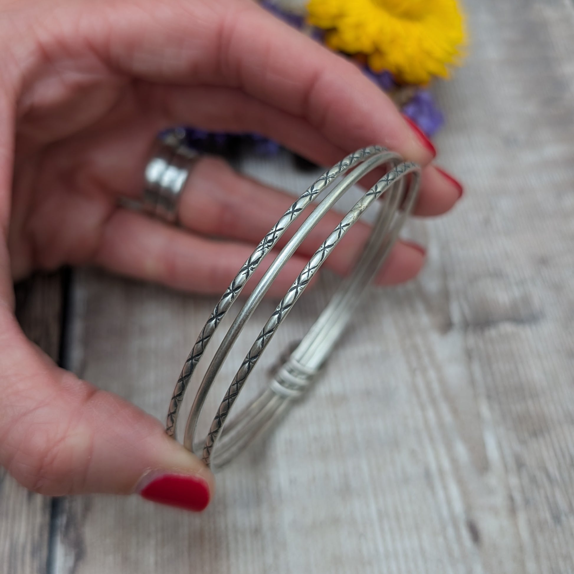 Three Sterling Silver bangles, one patterned, one smooth, one patterned passing through three silver open circles that move independently around the bangles.
