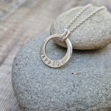 Load image into Gallery viewer, Sterling Silver ‘WARRIOR’ necklace. Silver disc with offset hole in centre, looks like a thick circle. Attached via two small silver hoops to silver chain. On thicker part of disc, inscription wording hammered into the silver reads WARRIOR in capitals. Disc measures approximately 20 mm in diameter. Chain length 16, 18 or 20 inches.