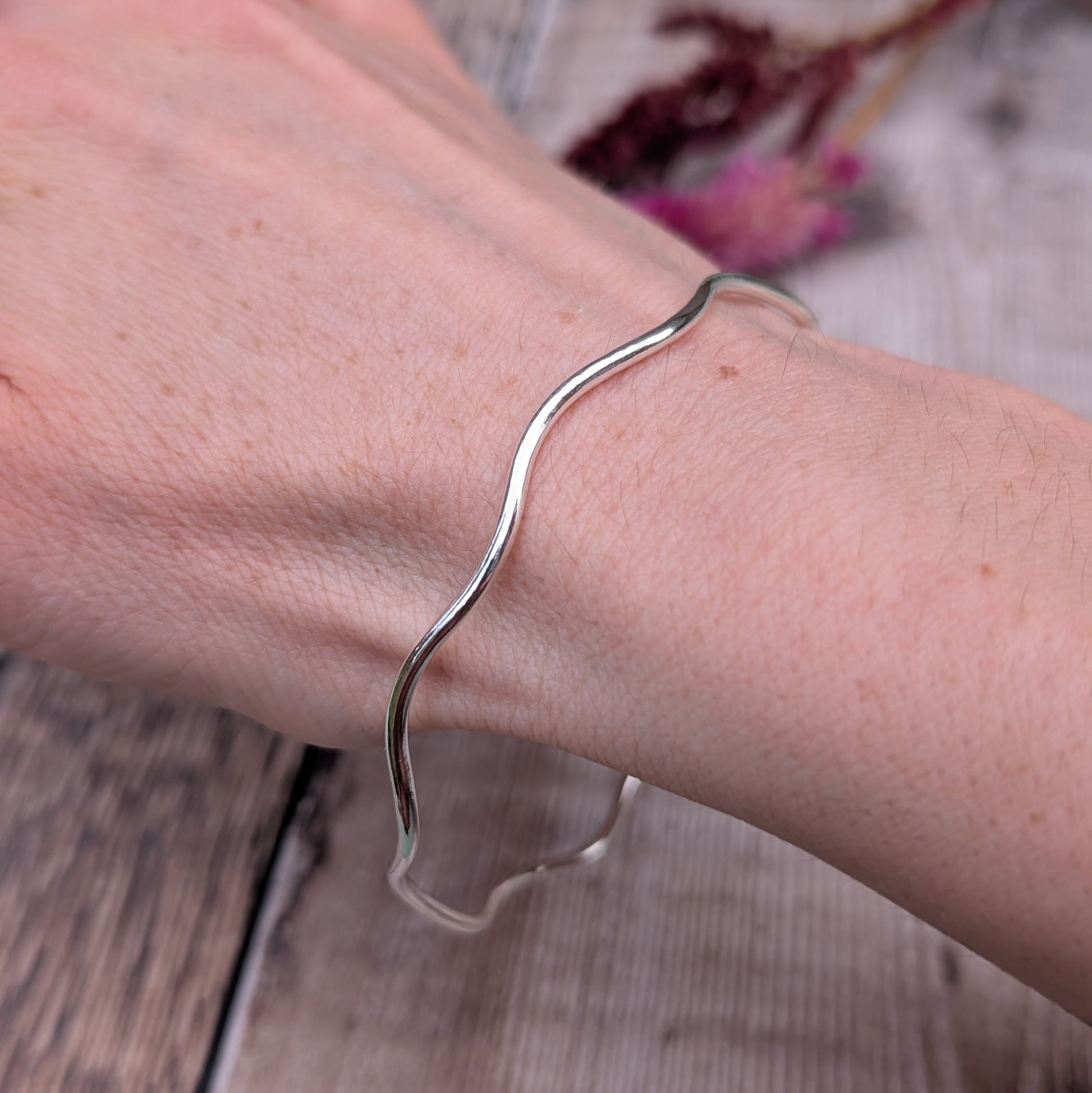 A recycled sterling silver wavy bangle worn on a wrist, highlighting its fluid shape and comfortable fit.