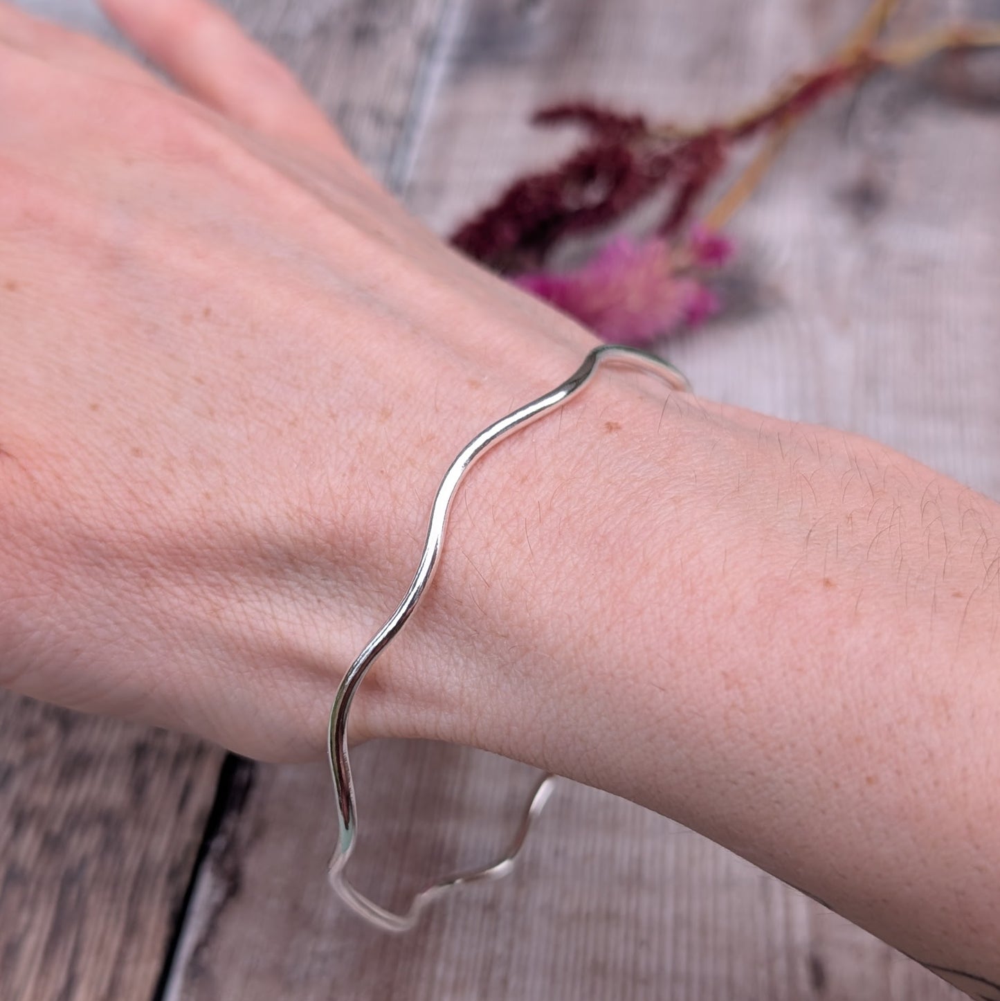 A recycled sterling silver wavy bangle worn on a wrist, highlighting its fluid shape and comfortable fit.