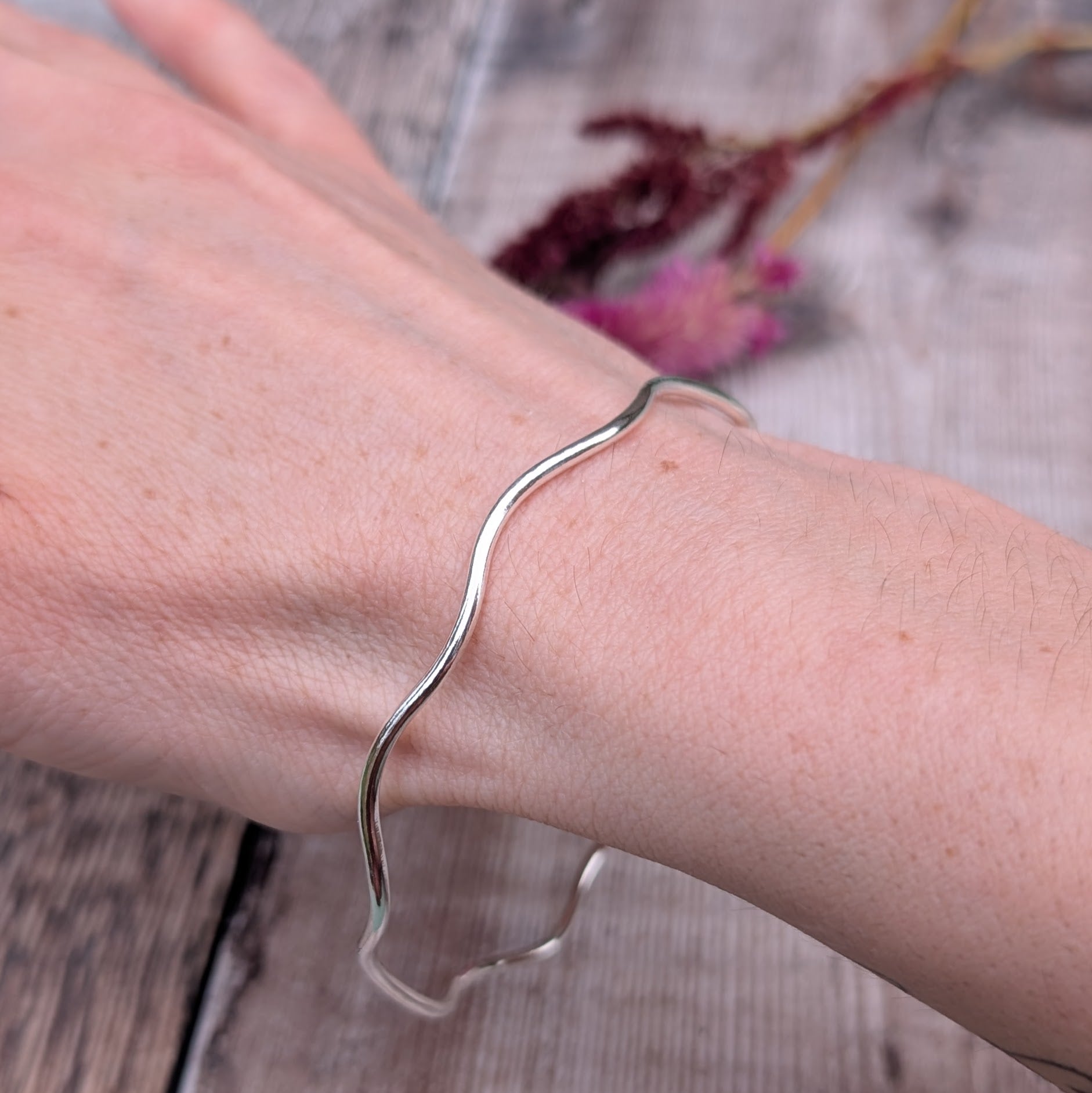 A recycled sterling silver wavy bangle worn on a wrist, highlighting its fluid shape and comfortable fit.