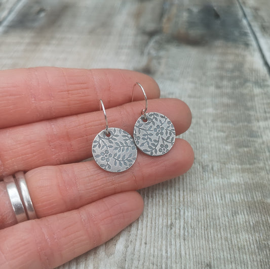 Each earring is a Sterling Silver disc stamped with a floral pattern of flowers with 5 petals and leaves suspended from silver earring wire.